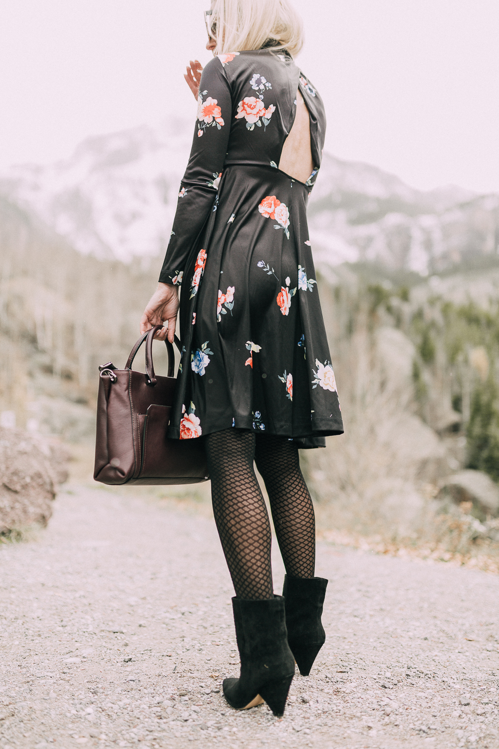 back of woman wearing regina black suede Booties by Vince Camuto paired with black open-back floral print dress and burgundy tote bag