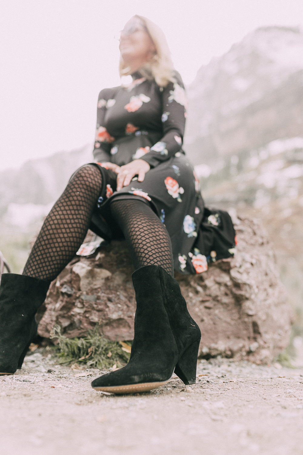 woman sitting on rock wearing regina vince camuto black suede booties and black print floral dress