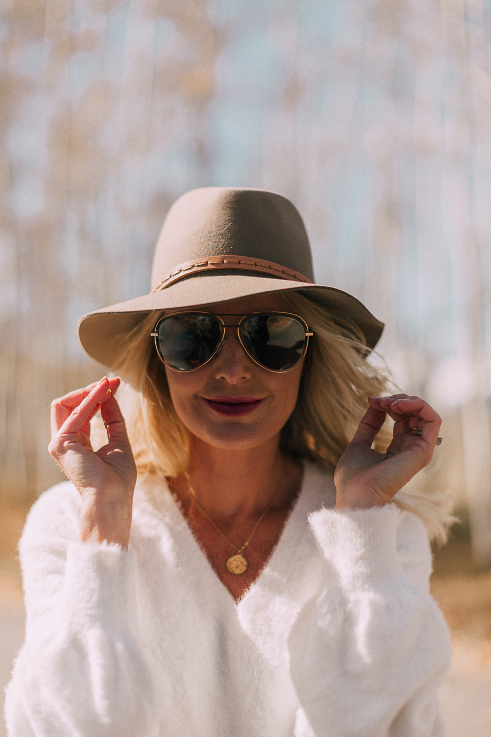 blonde woman wearing rag & bone hat, sunglasses, white sweater, and gold necklace