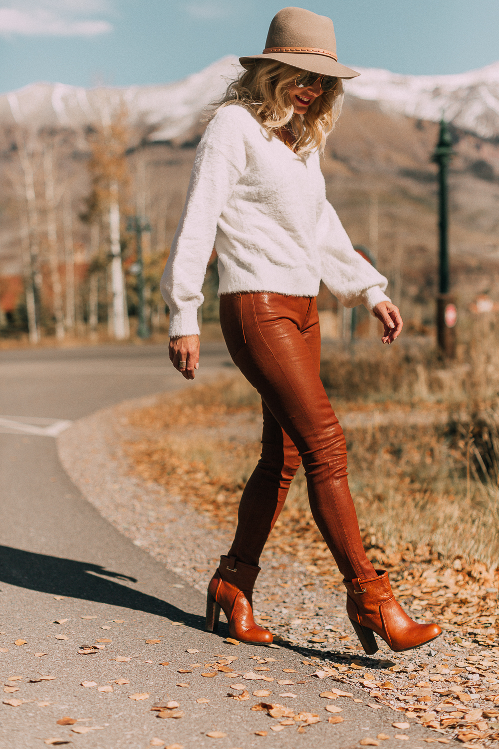 Blonde woman in Telluride, Colorado wearing brown leather pants by Frame with a white fuzzy Halogen sweater, Saint Laurent boots, and a rag & bone hat, sharing how to wear leather pants