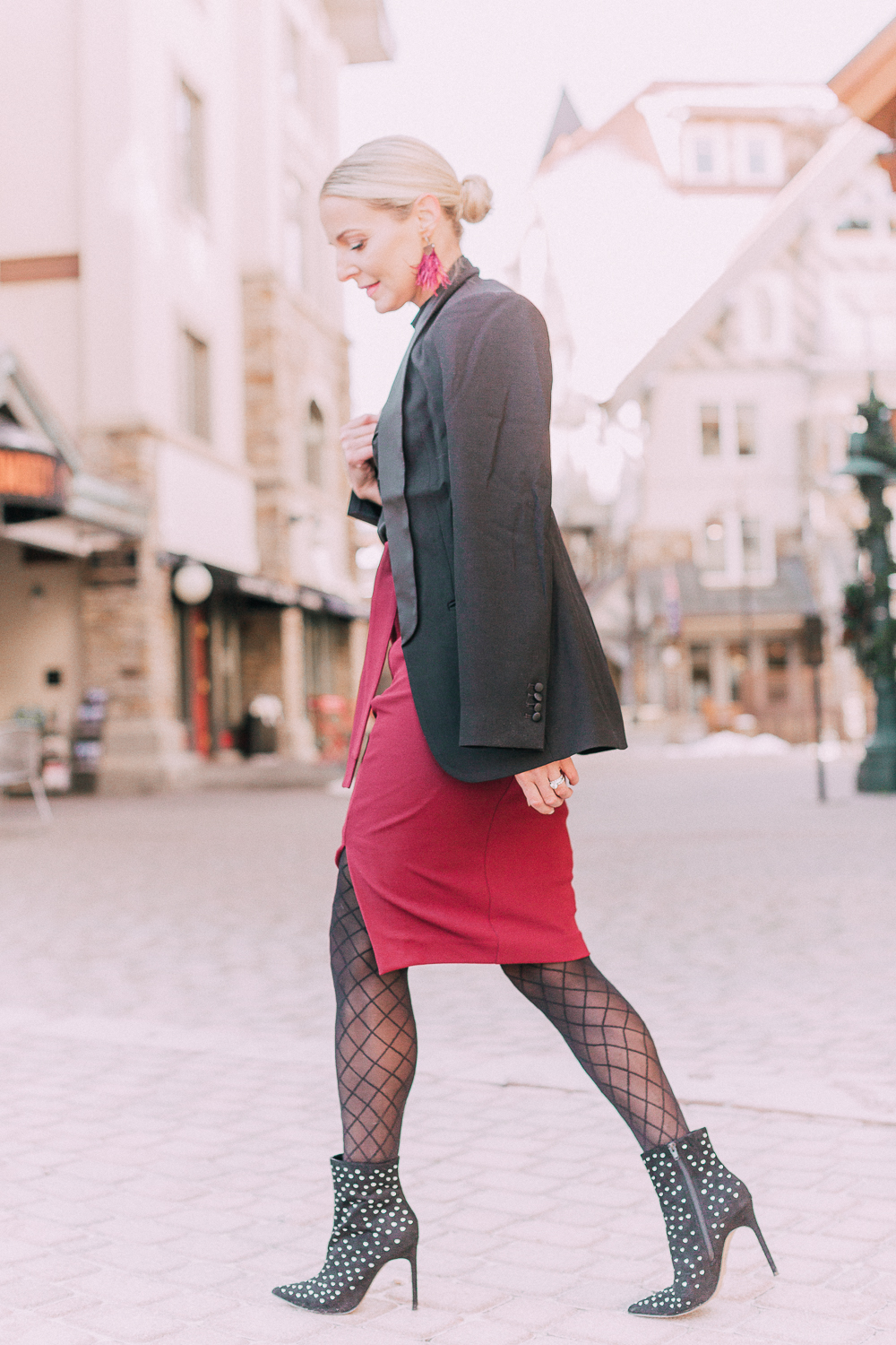 What to wear to a holiday party when it's cold outside, featuring a burgundy pencil skirt, black silky tie neck blouse, black diamond print tights, crystal studded ankle booties, and a black tuxedo blazer from Express