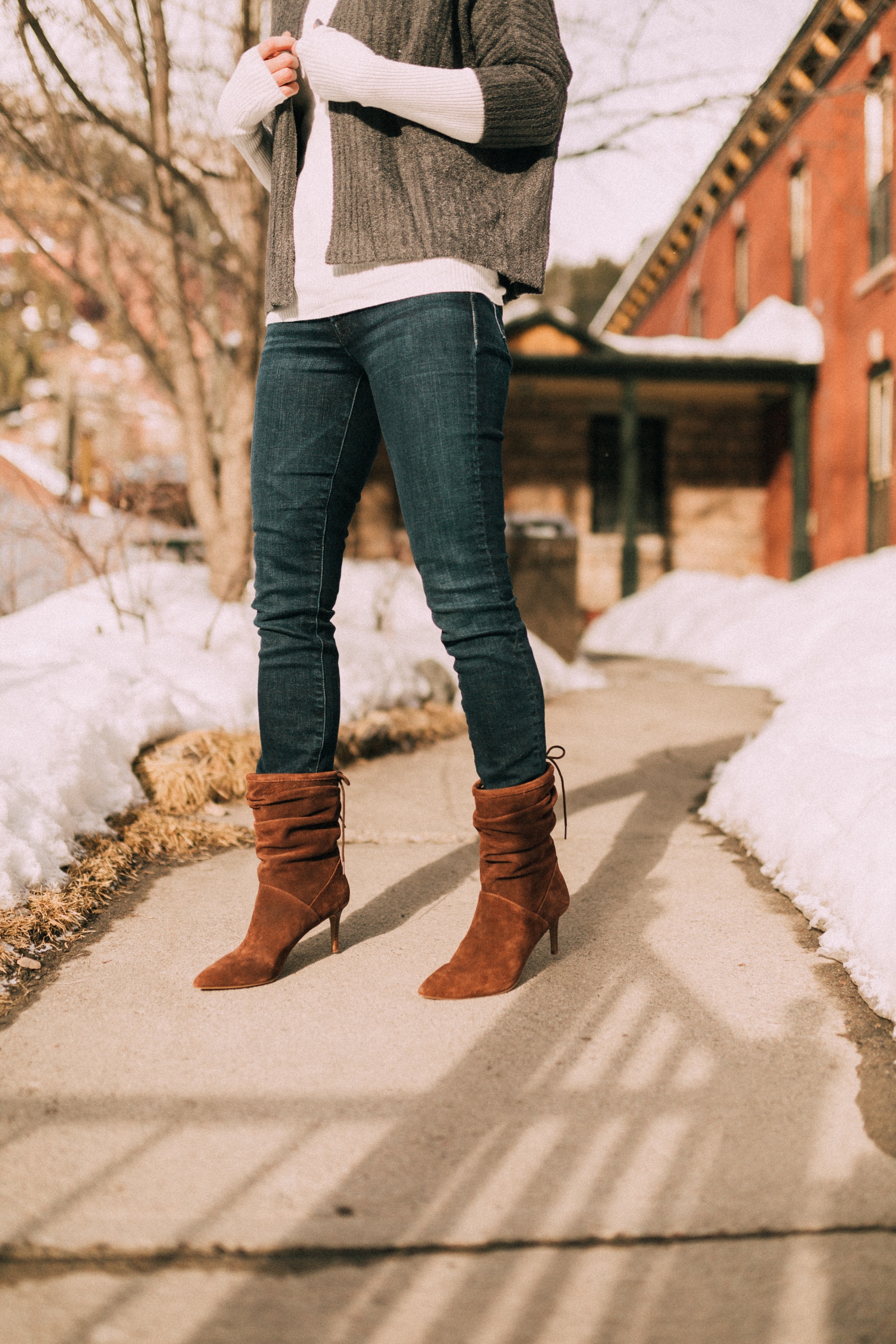 Fashion blogger Erin Busbee of BusbeeStyle.com wearing brown heeled booties from QVC with dark wash skinny jeans, a white turtleneck, and barefoot dreams shrug cardigan