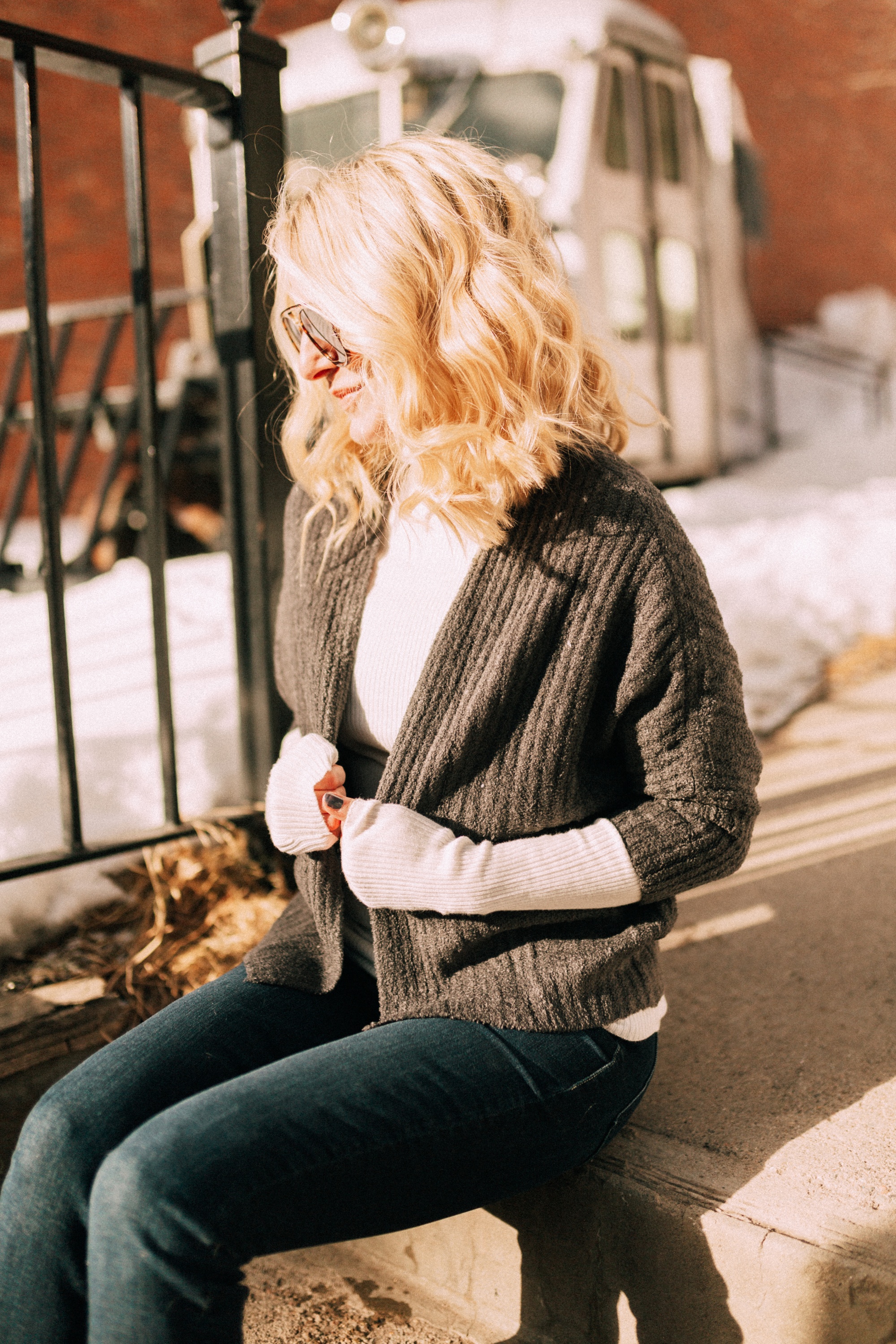Blonde fashion blogger Erin Busbee of Busbee Style sitting in Telluride, Colorado wearing a Barefoot Dreams shrug with a white turtleneck and dark wash skinny jeans