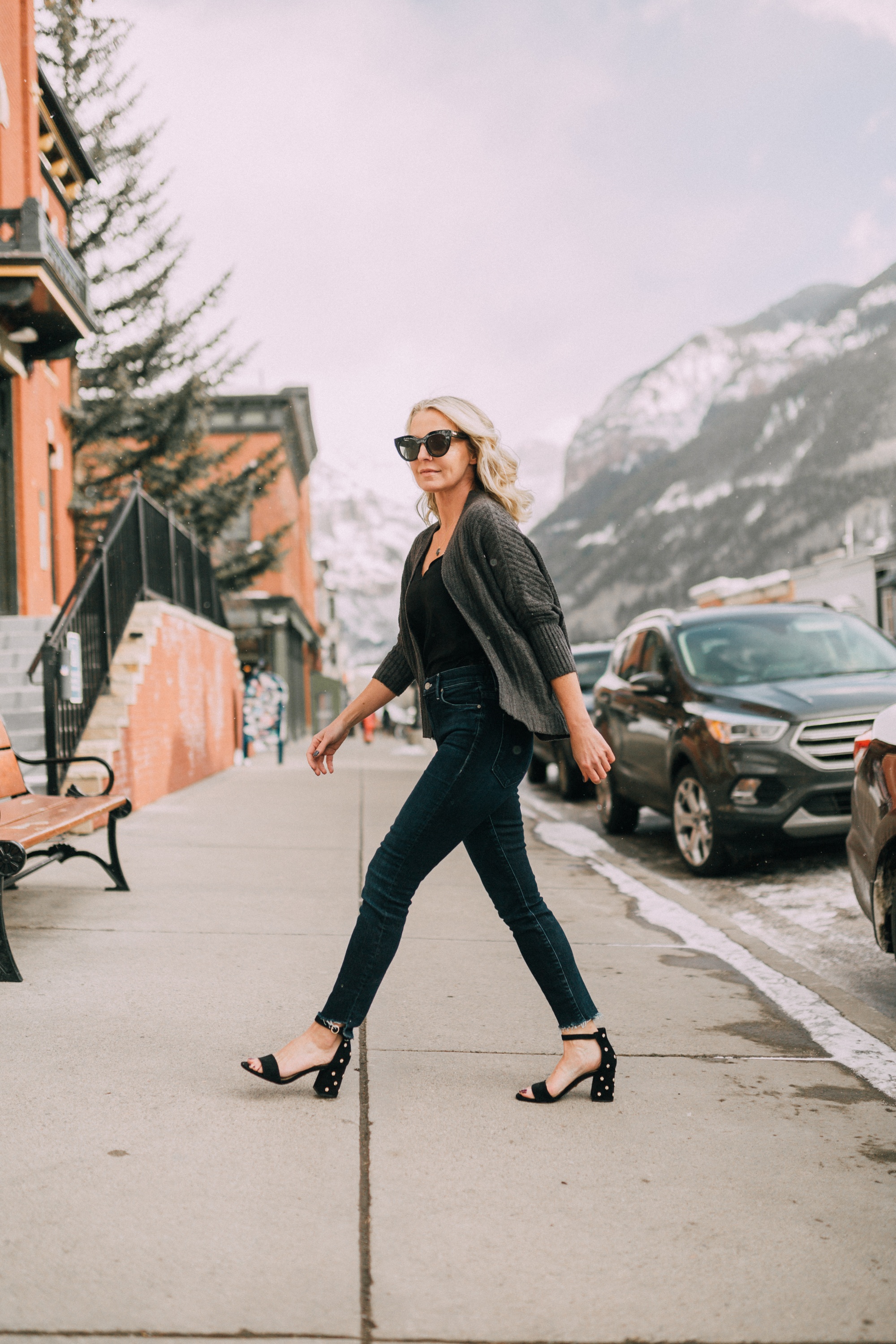Fashion blogger over 40 Erin Busbee of busbeestyle.com wearing dark wash skinny jeans, a black scalloped cami, and heeled black sandals with a Barefoot dreams shrug from QCV, walking in Telluride, Colorado