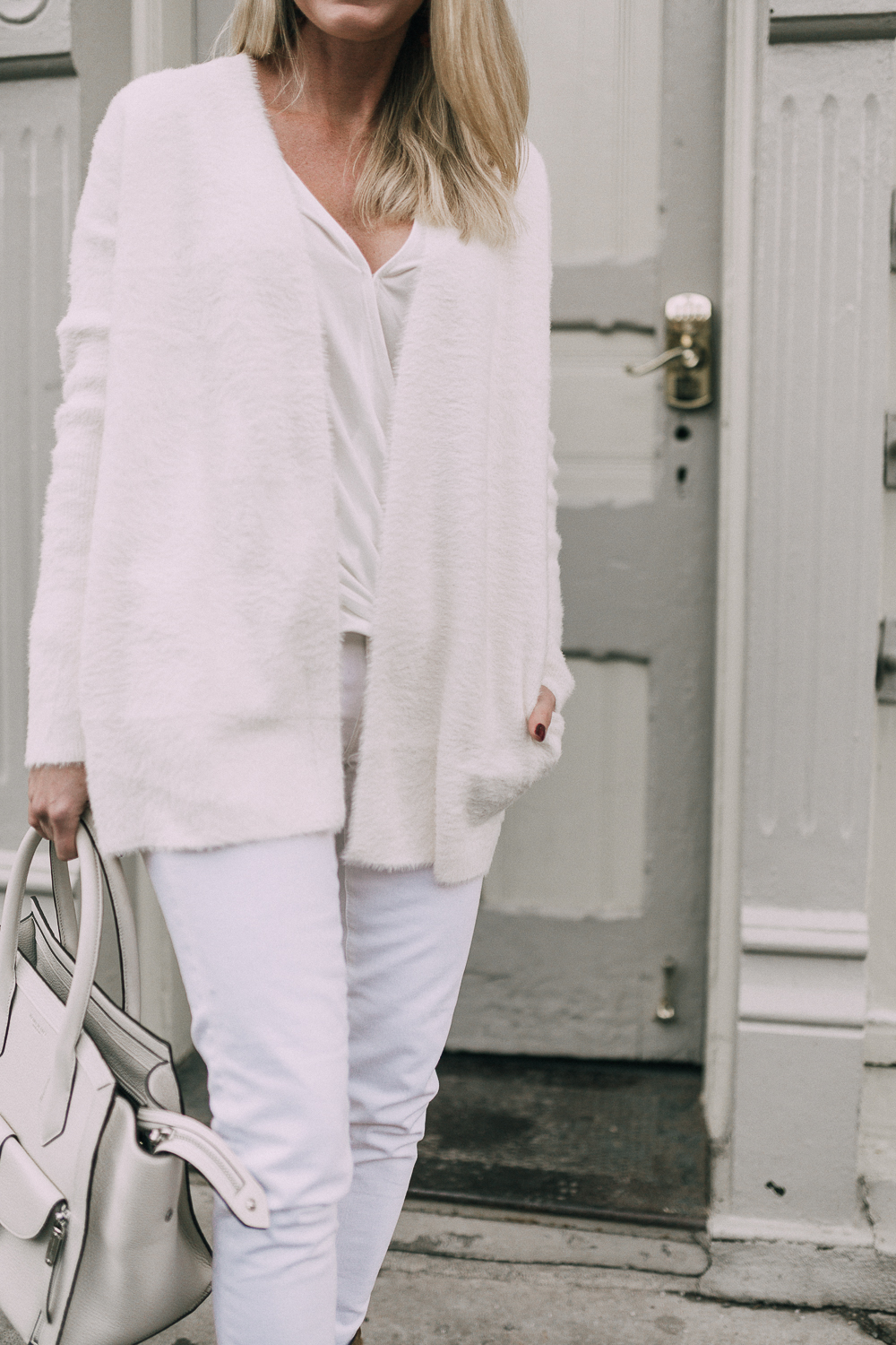 Fashion blogger Erin Busbee of BusbeeStyle.com sharing a winter white look with a Banana Republic cardigan, white jeans, white wrap front top, and white Henri Bendel bag