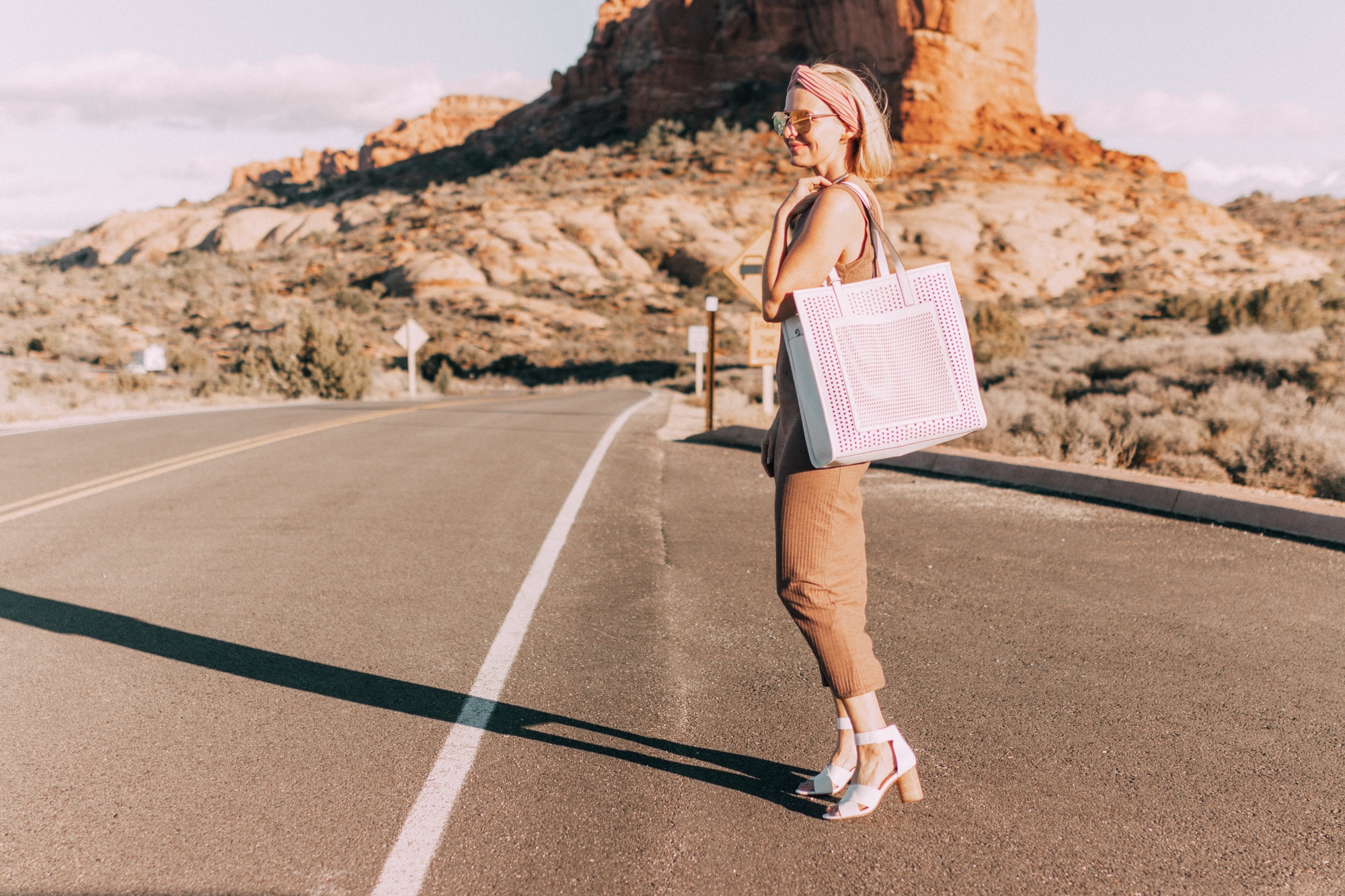Spring Handbags, Fashion blogger Erin Busbee of BusbeeStyle.com wearing a brown sweater dress by David Lerner from Revolve, a white perforated tote bag fromVince Camuto, and white ankle strap sandals from Vince Camuto in Moab, Utah