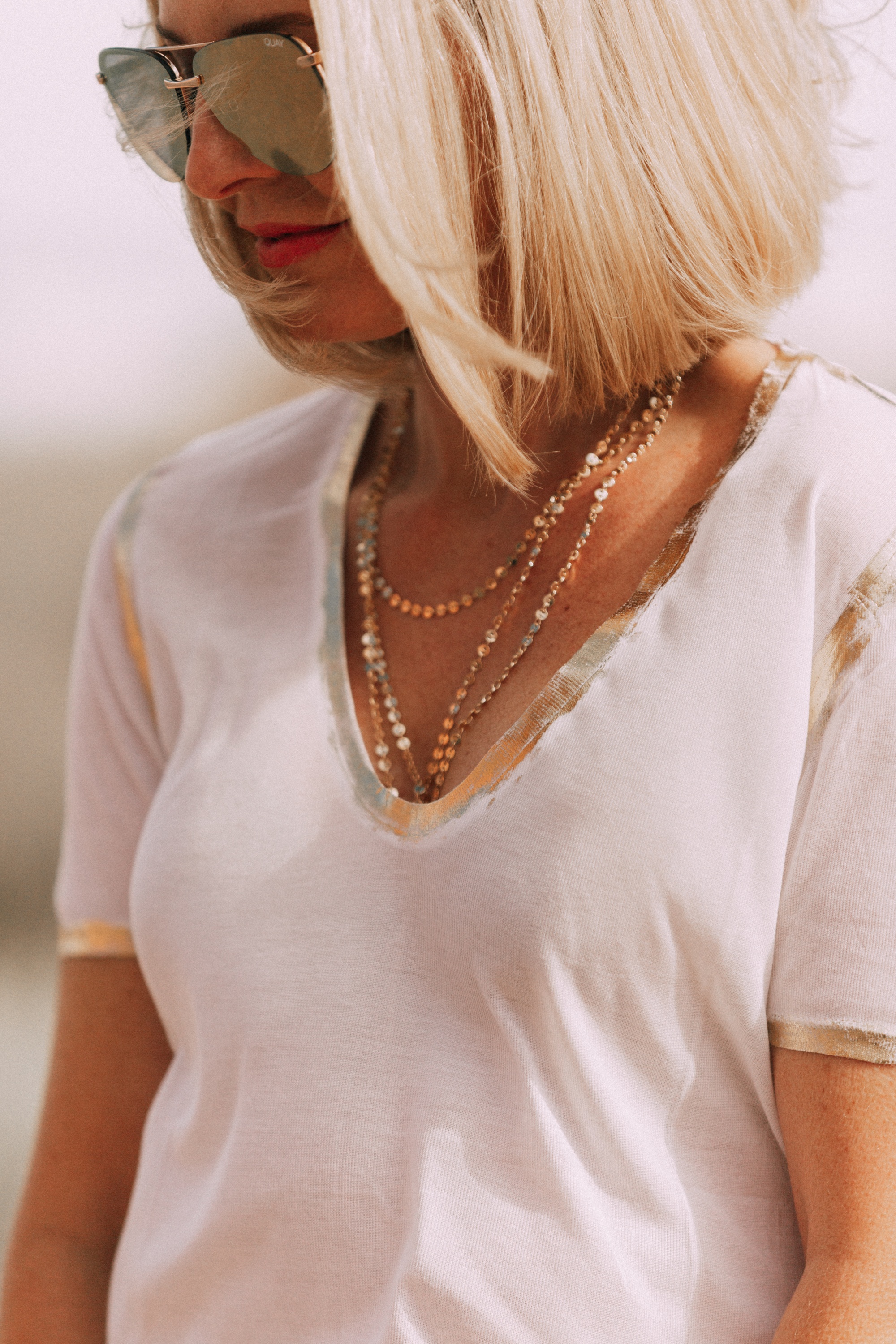 close up of zadig & voltaire metallic trim v neck tee shirt worn with dainty gold necklace and sunglasses