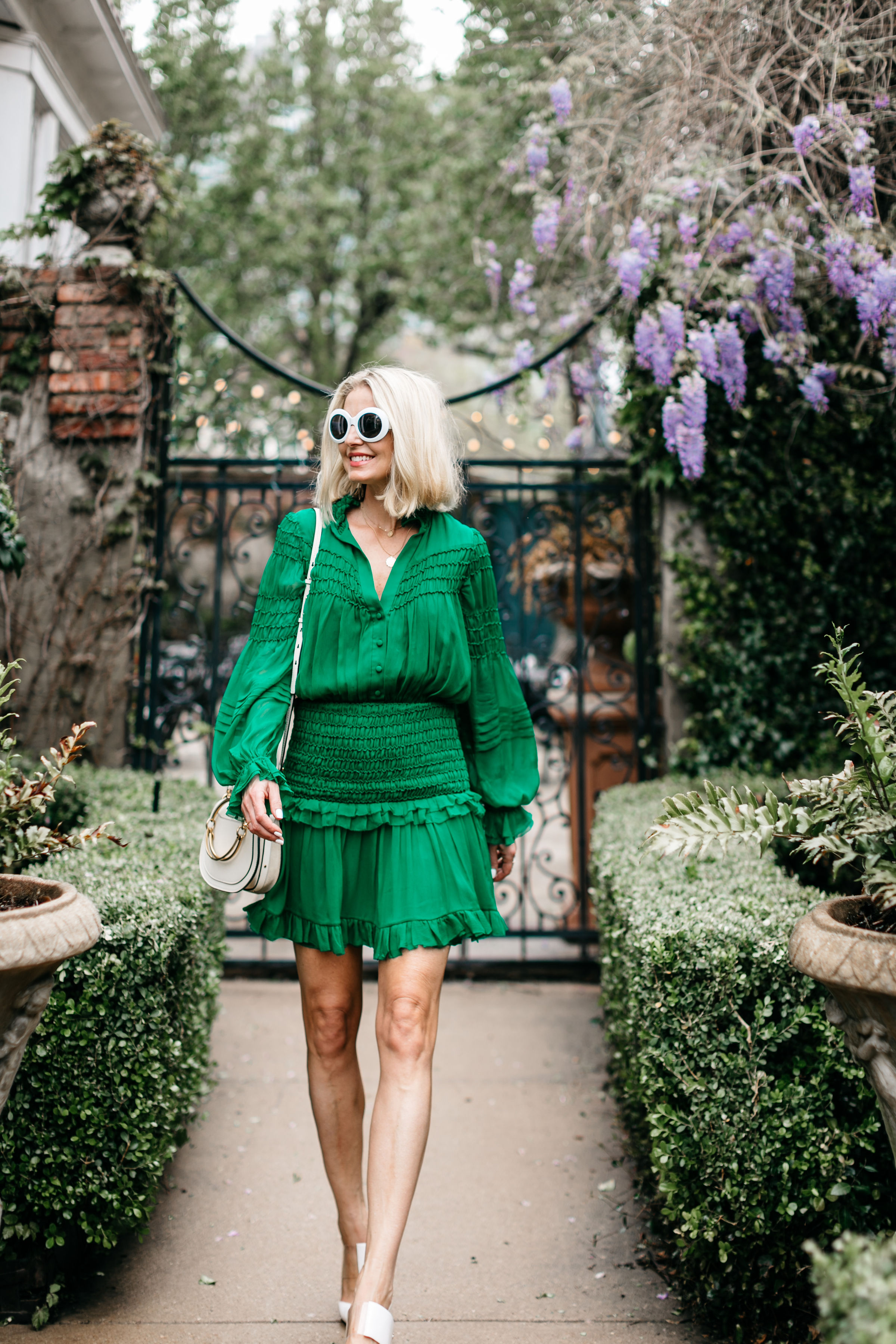fashion blogger wearing kelly green silk mini dress with white sam edelman heels carrying chloe nile small bracelet bag in a garden