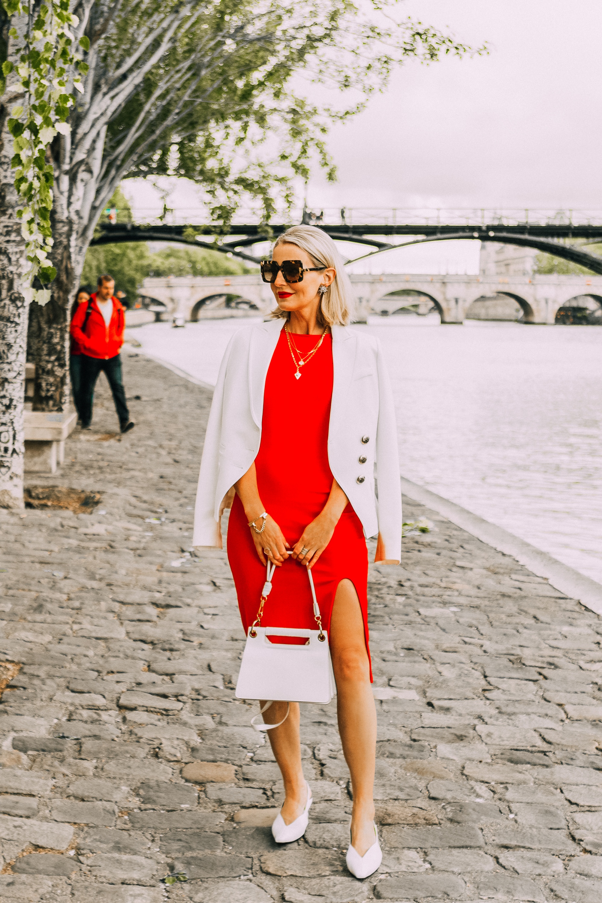 erin busbee wearing red midi length sheath dress with slit with ivory smythe wrap blazer draped over shoulders paired with white slingback heeled mules carrying white calfskin givenchy whip bag