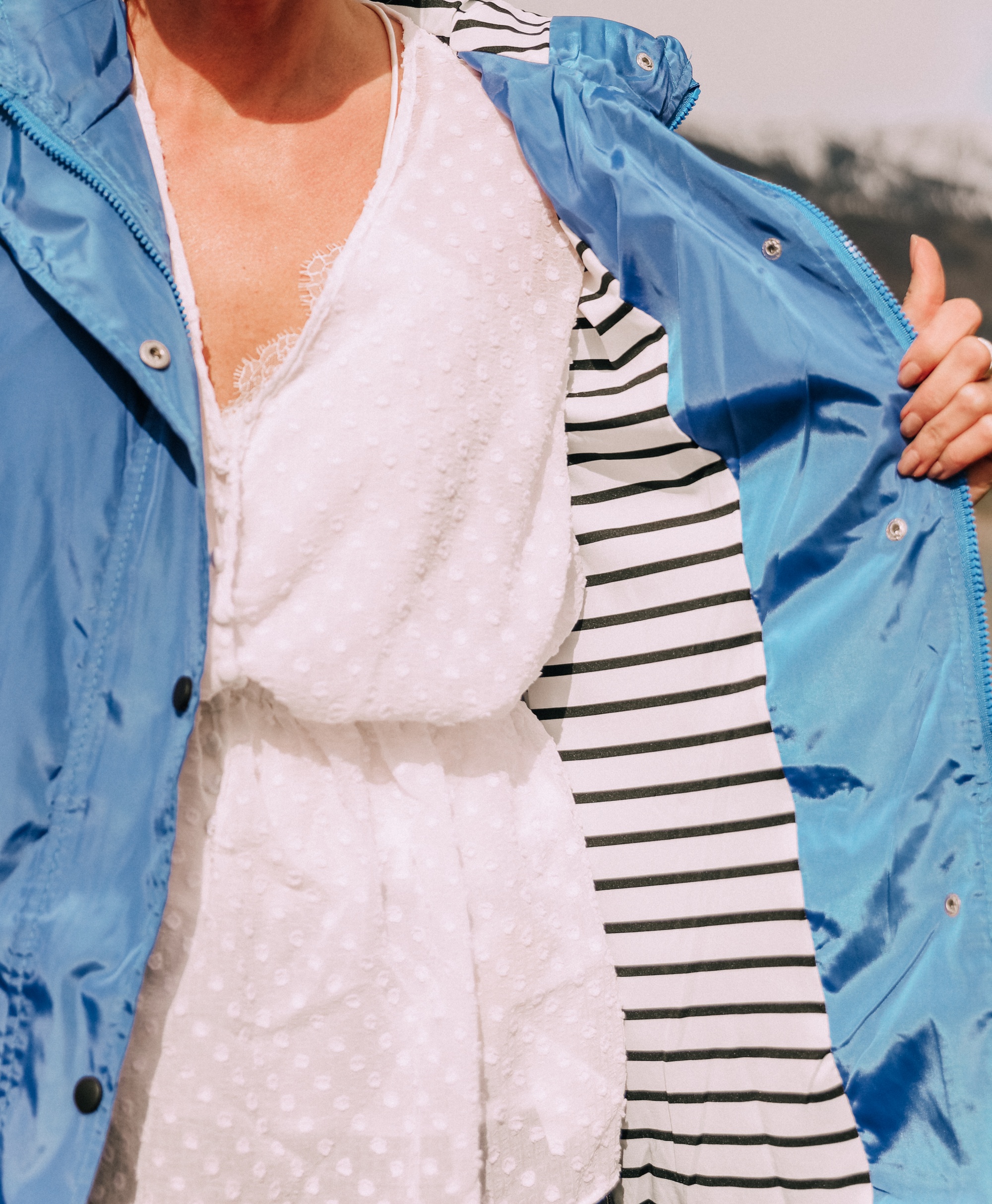 affordable blue waterproof lightweight raincoat with black and white striped lining over white cinched blouse