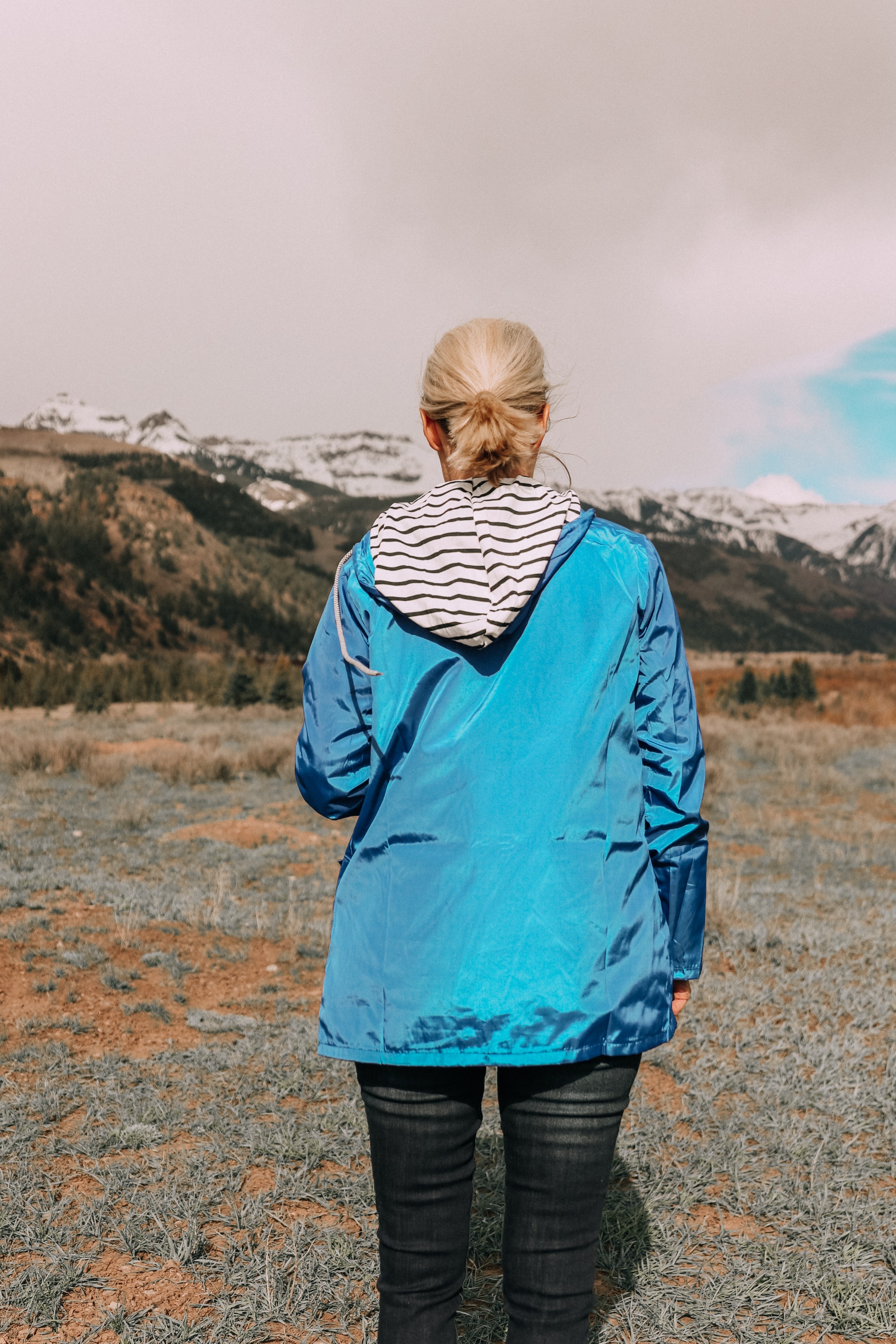 backside of fashion blogger in telluride colorado wearing affordable blue waterproof lightweight raincoat with black and white striped hood paired with dark wash jeans