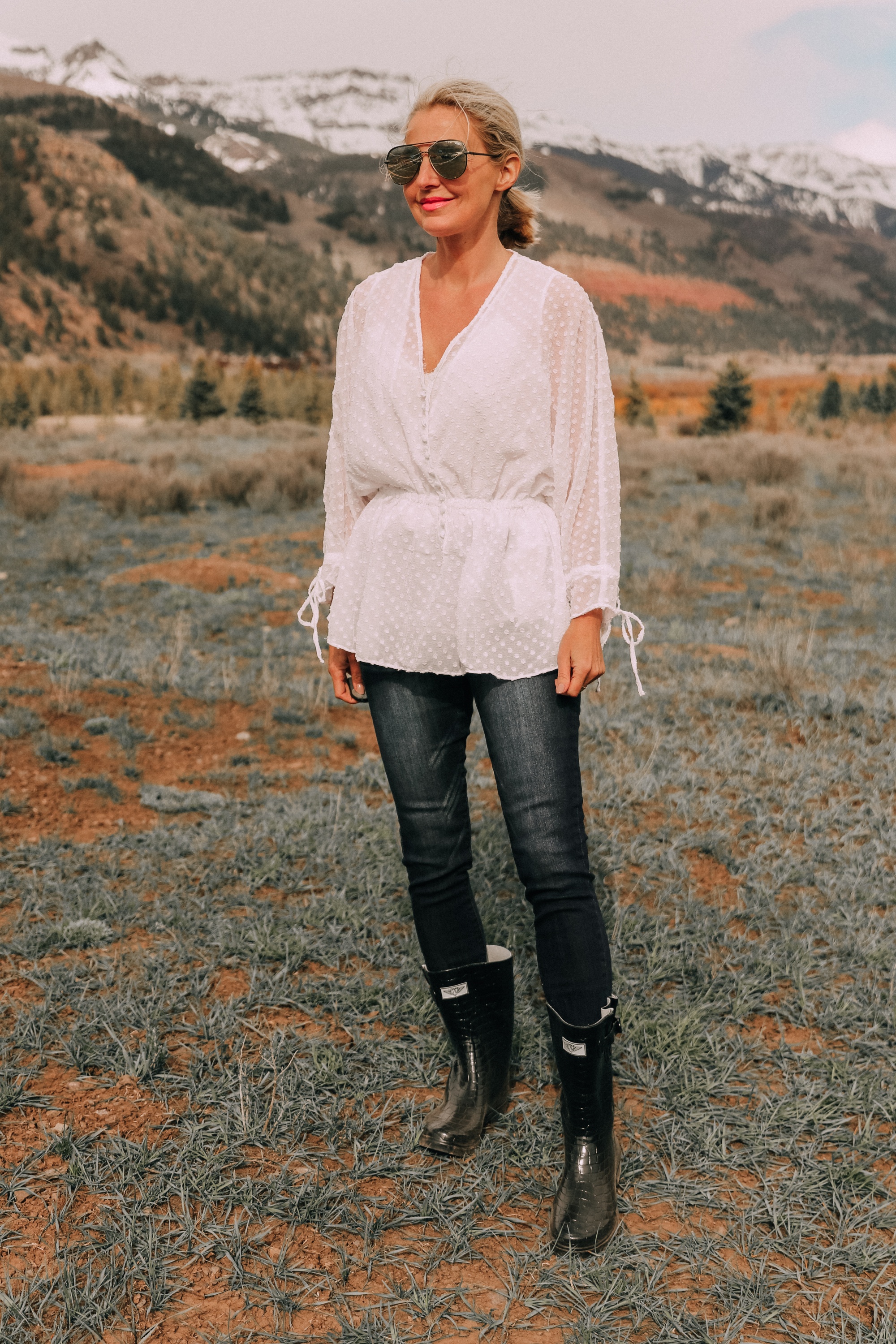 fashion blogger erin busbee in telluride colorado wearing white cinched blouse paired with dark wash skinny ankle jeans styled with croc patterned rubber rain boots