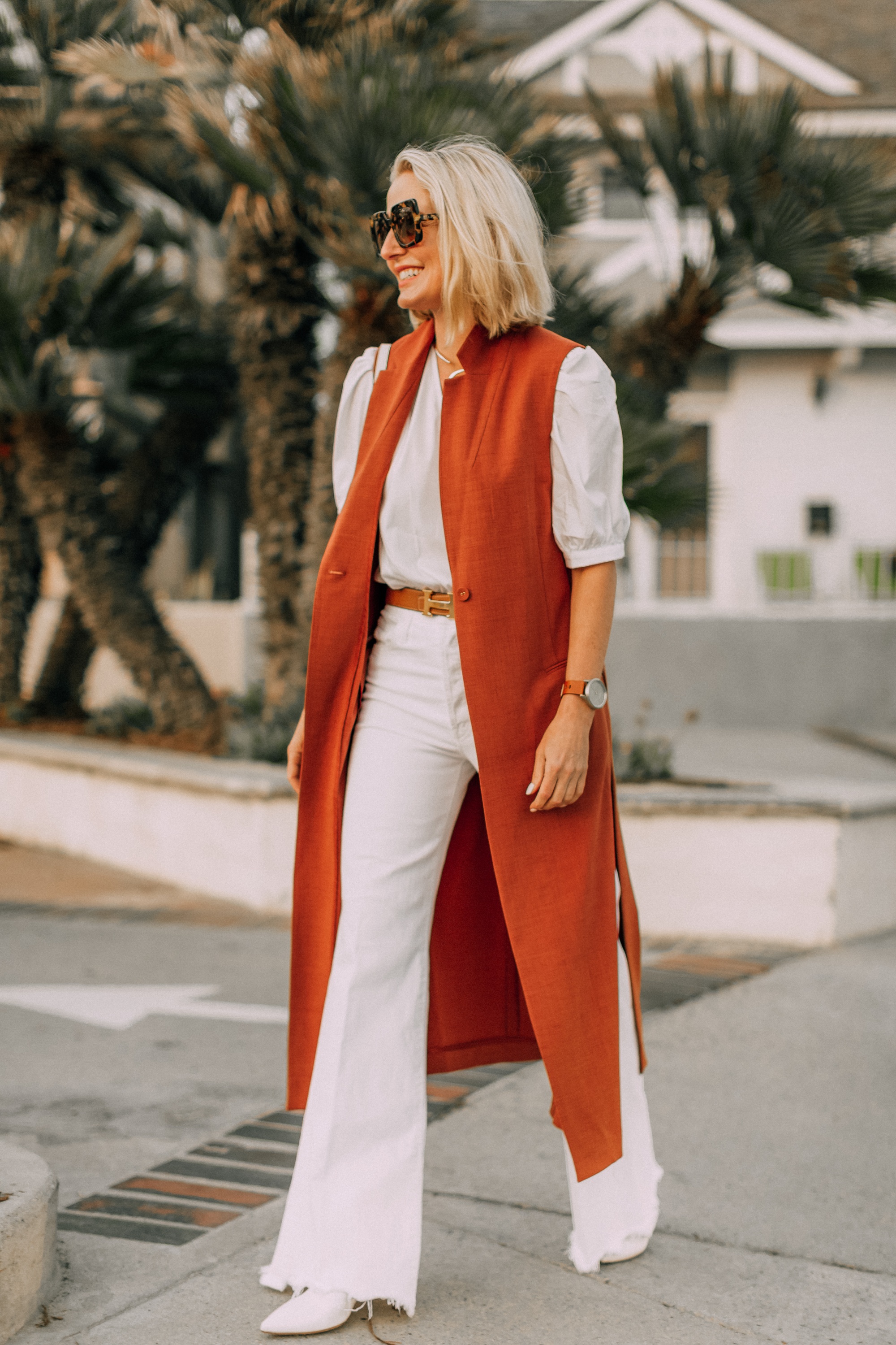 fashion blogger busbee style showing how to wear a long rust colored vest in cute all white outfit