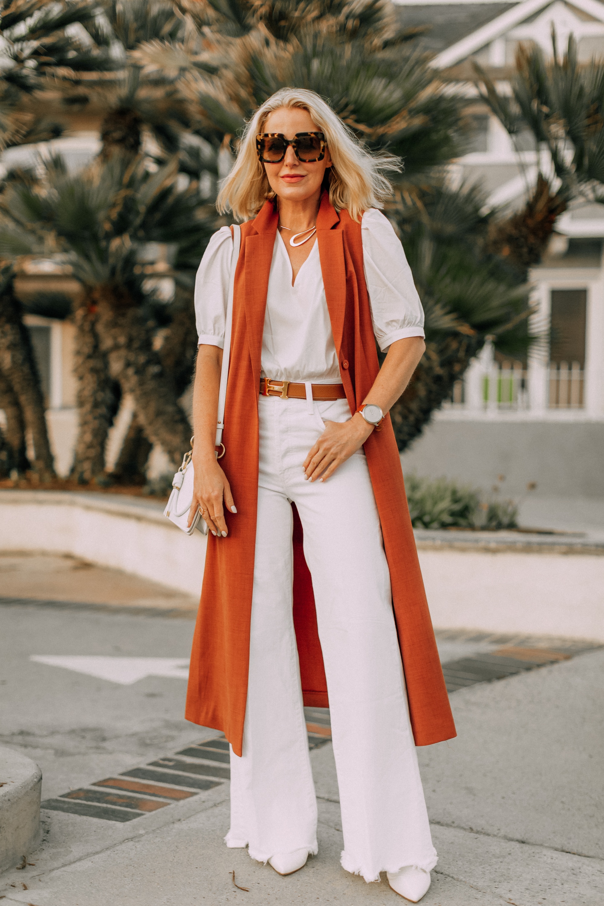 fashion blogger busbee style showing how to wear long vest with all white outfit and hermes belt