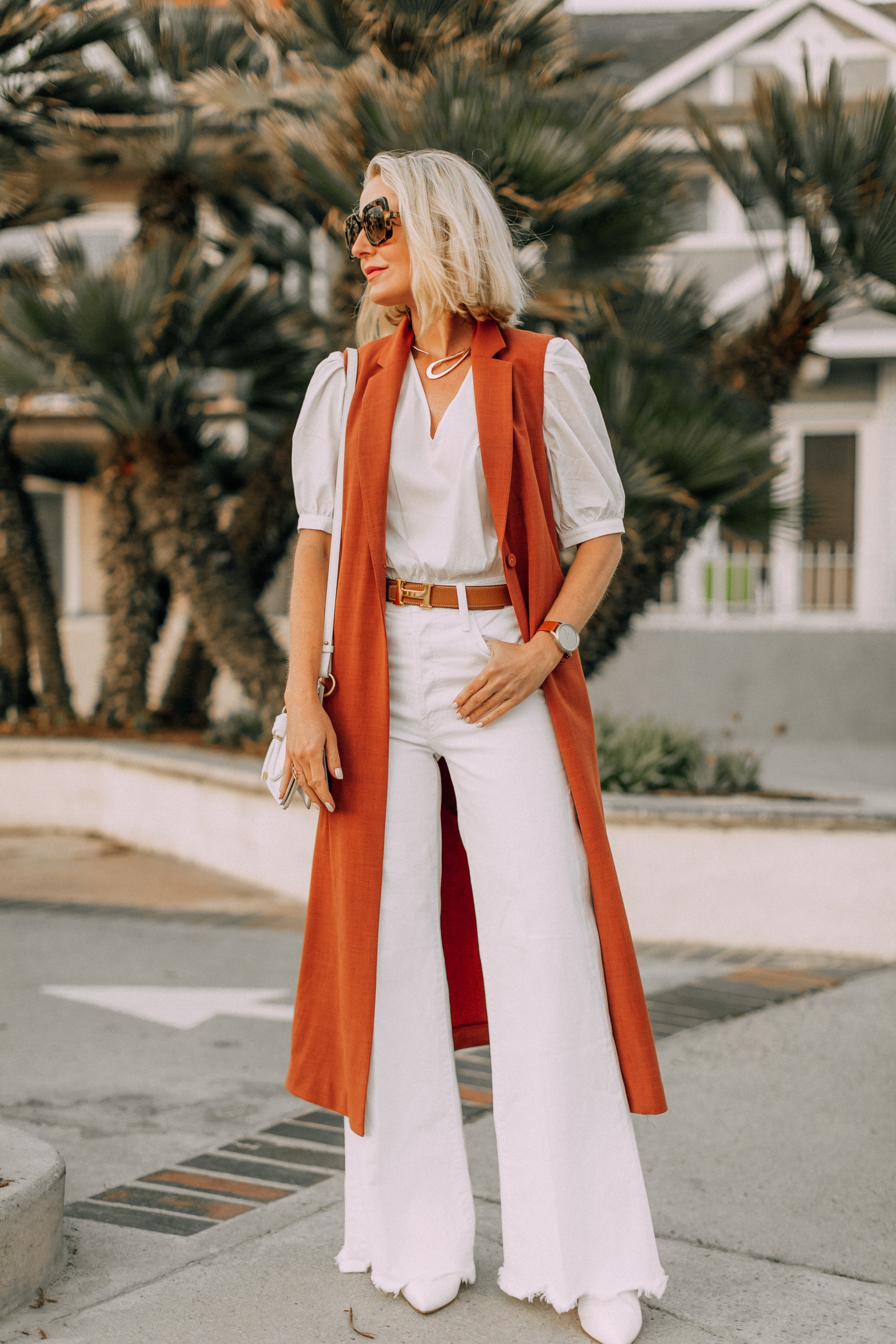fashion blogger busbee style showing how to wear long vest with all white outfit and hermes belt