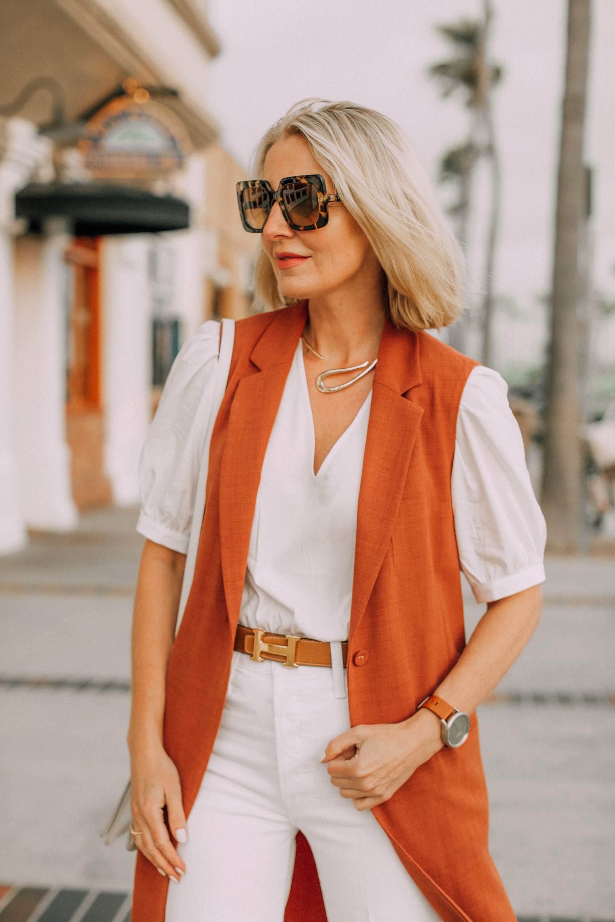 fashion blogger busbee style showing how to wear long rust color BCBG vest with white jeans and hermes belt