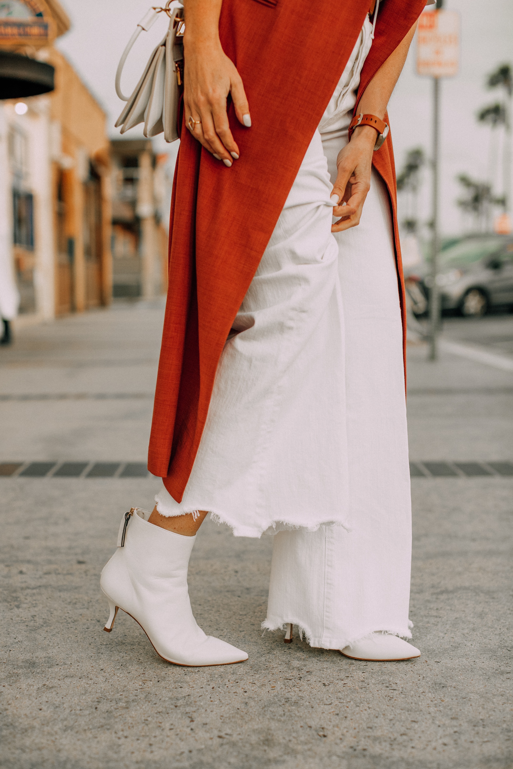 fashion blogger wearing stuart weitzman white juniper 70 pointed toe booties with long rust colored vest