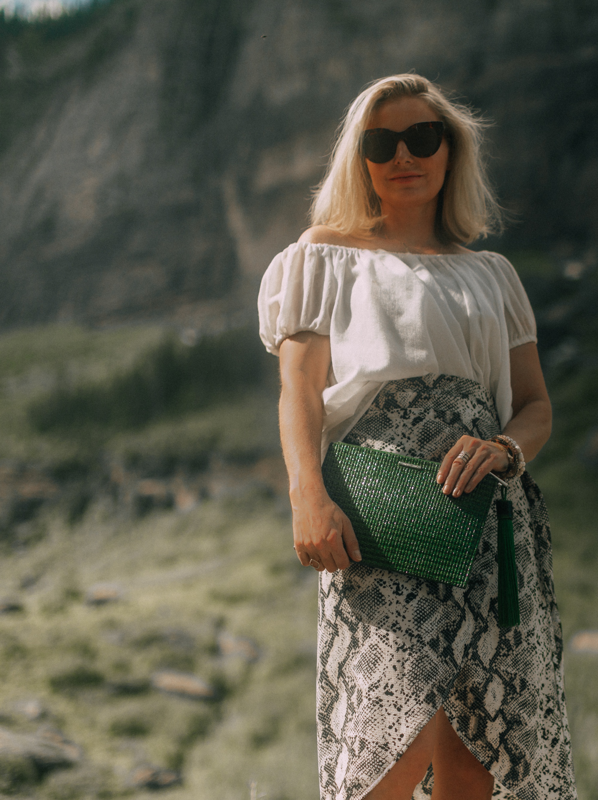Styling animal print clothes with neutral Accessories, Fashion blogger Erin Busbee of BusbeeStyle,com wearing metallic gold croc-embossed sandals and green clutch from Vince Camuto with a white off the shoulder top and python print wrap skirt from Evereve in Telluride, CO