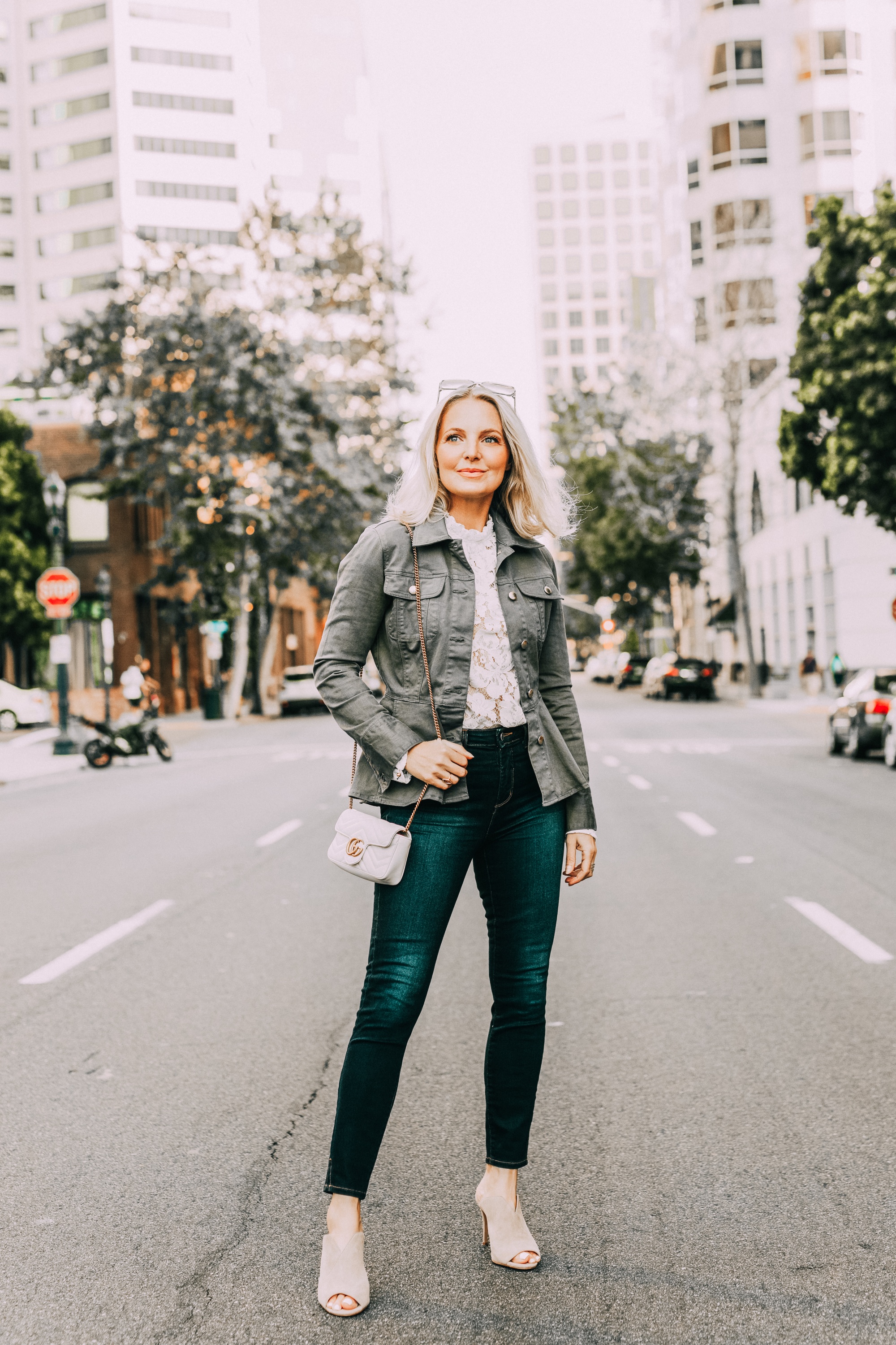 https://rstyle.me/+G549sNdFdbDQEUhaXWr8KQ, White Top Under $100, Fashion blogger Erin Busbee of BusbeeStyle.com wearing a white lace top by WAYF with dark wash skinny jeans by L'AGENCE, neutral Vince Camuto peep-toe mules, a white mini Gucci bag, and green peplum Frame jacket in San Diego, California