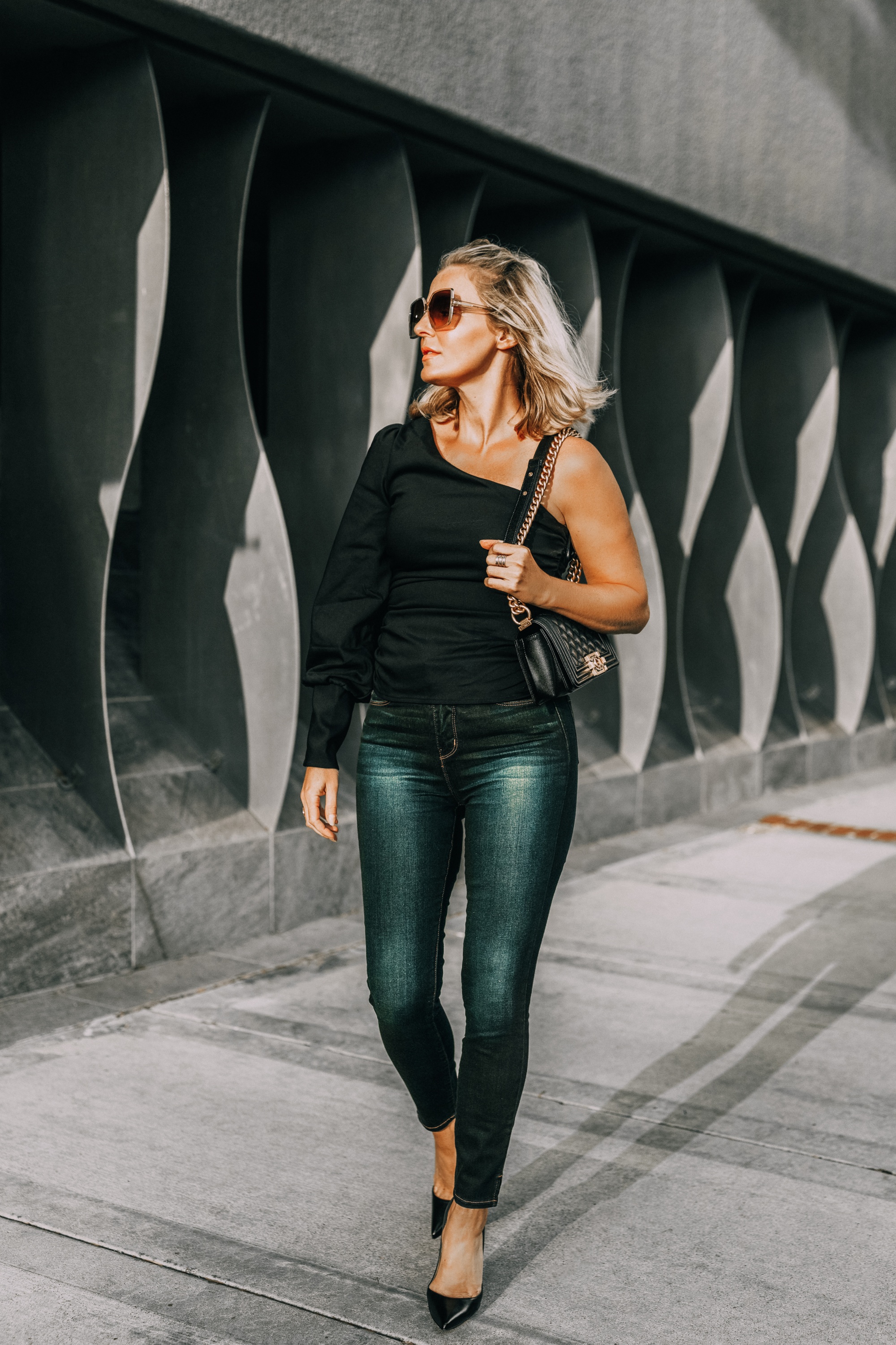 Sexy one-shoulder date night top for women over 40, easy date night outfit styled by fashion blogger over 40 Busbee Style with black shoulder baring l'Academie top, dark wash l'Agence skinny jeans, black Christian Louboutin pumps and quilted Chanel boy bag