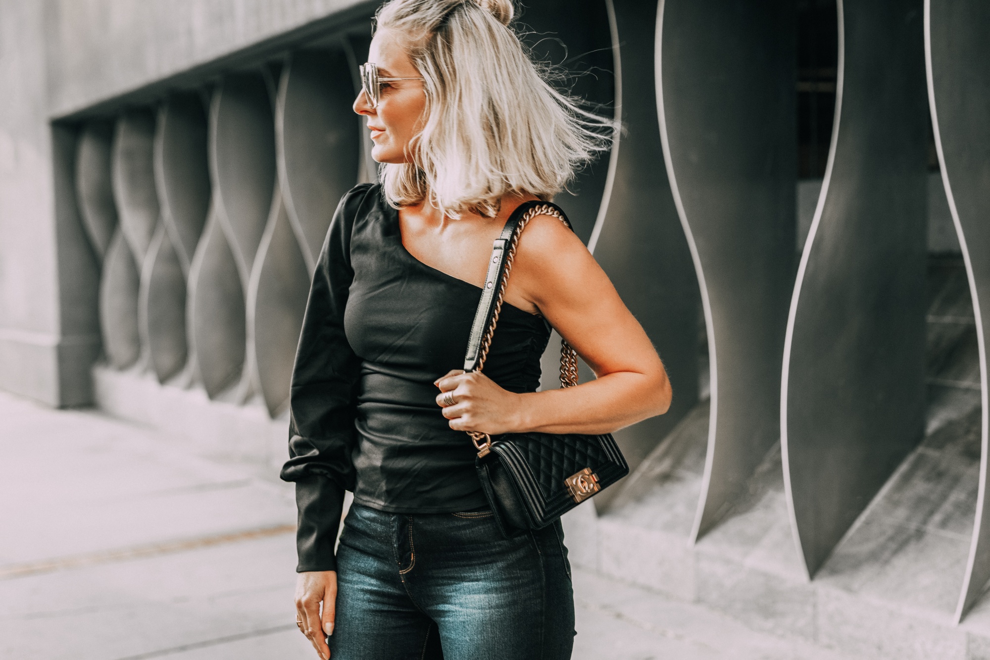 Sexy one-shoulder date night top for women over 40, easy date night outfit styled by fashion blogger over 40 Busbee Style with black shoulder baring l'Academie top, dark wash l'Agence skinny jeans, and quilted Chanel boy bag