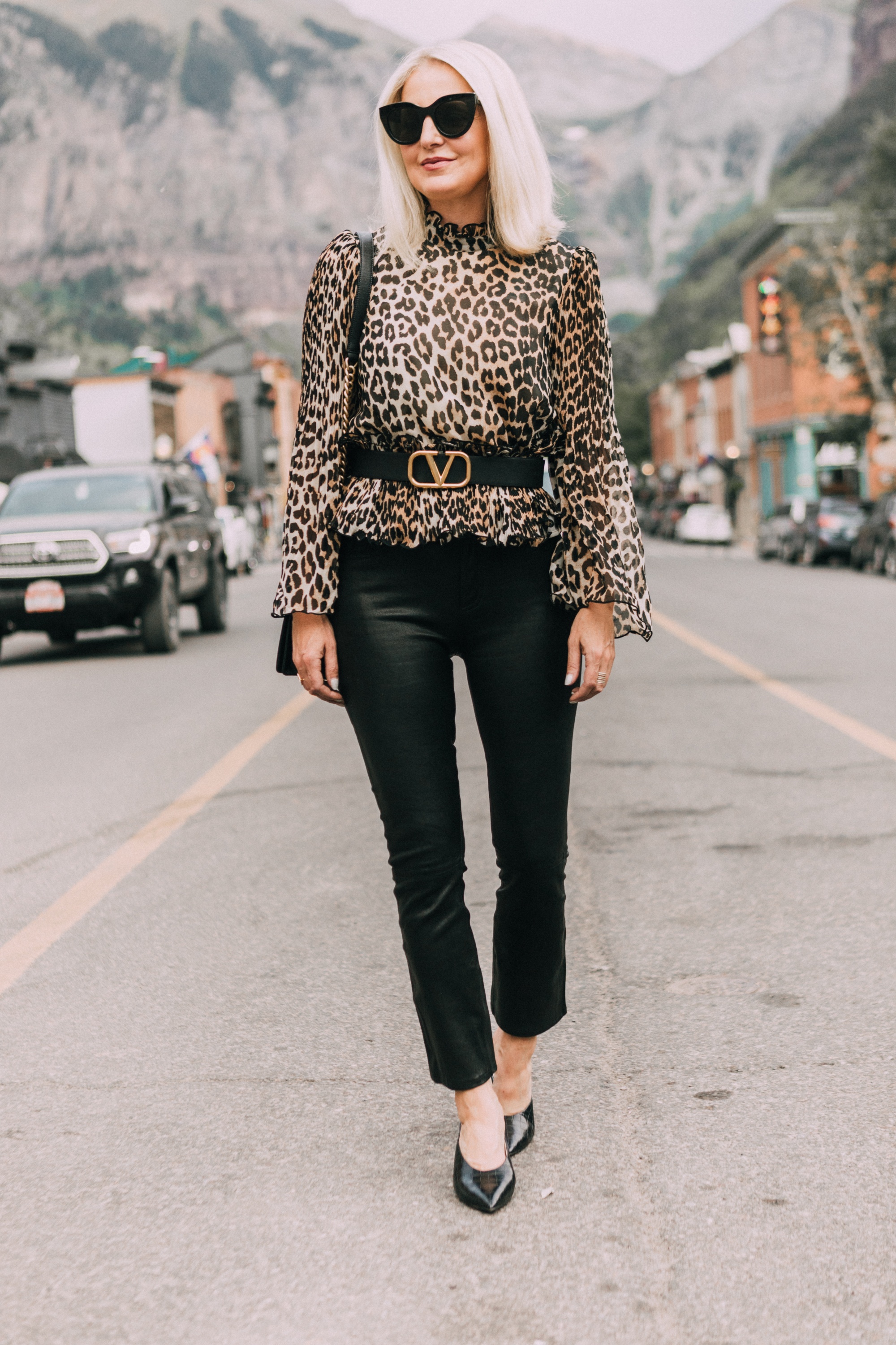 Hochgeschlossene Oberteile, Modebloggerin Erin Busbee von BusbeeStyle.com trägt eine hochgeschlossene Bluse mit Leopardenmuster von Ganni mit einer schwarzen Lederhose, einem Valentino-Gürtel und schwarzen Pantoletten mit Krokodilprägung in Telluride, CO