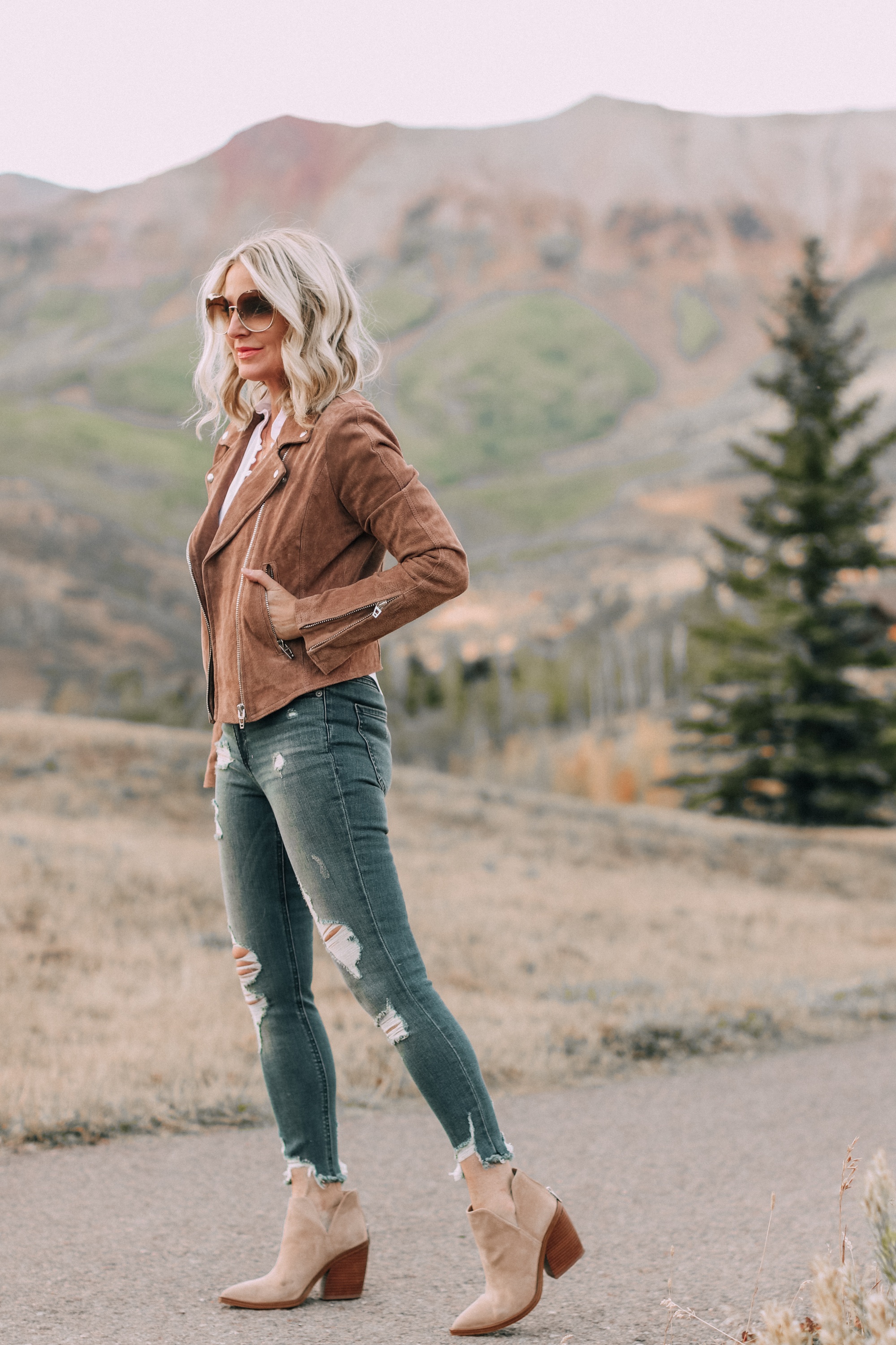 Blank NYC next level moto jacket on fashion blogger Erin Busbee of Busbee Style paired with Express white blouse and distressed jeans with beige Vince Camuto booties and Chloe sunglasses in Telluride, Colorado