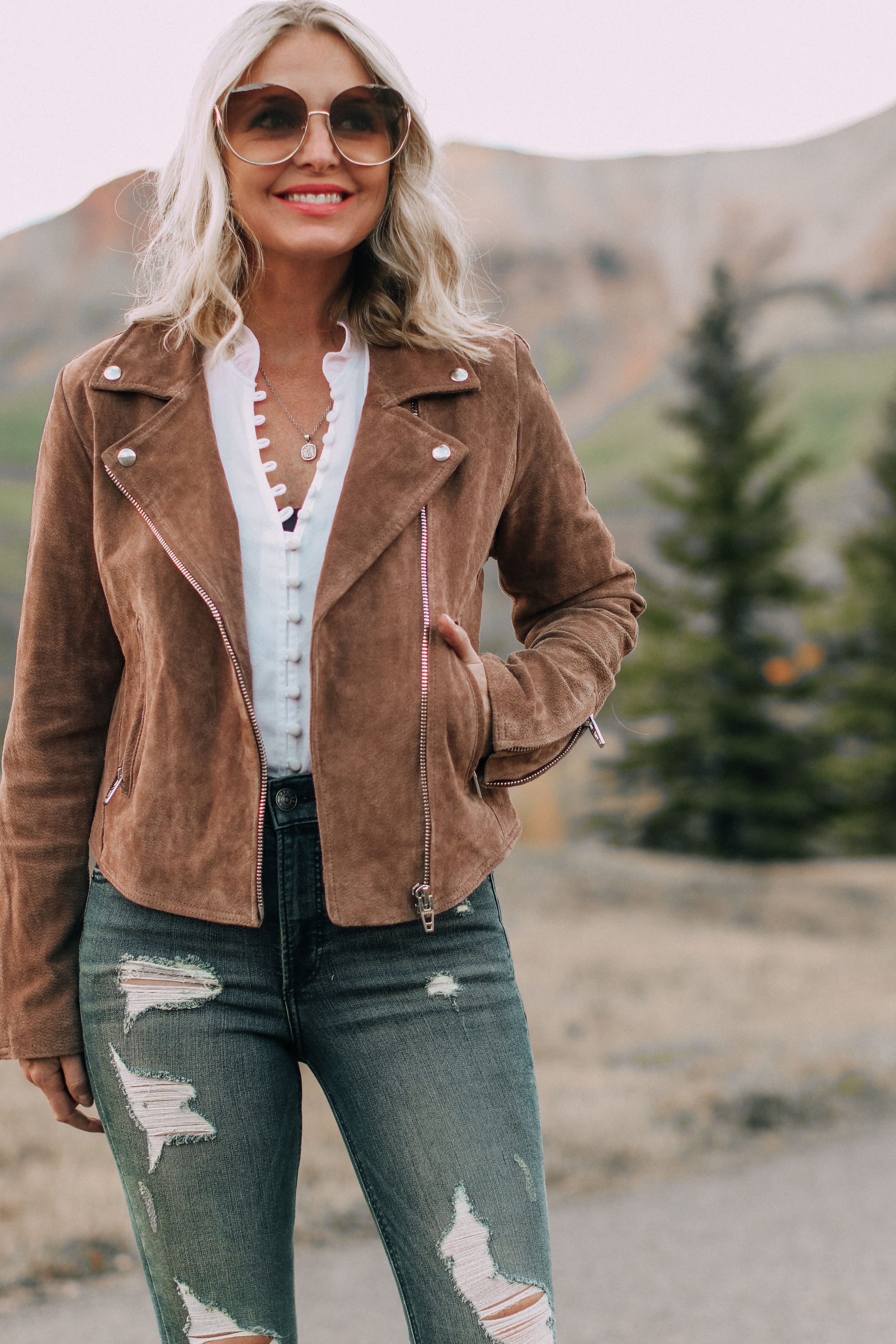 Blank NYC next level moto jacket on fashion blogger Erin Busbee of Busbee Style paired with Express white blouse and distressed jeans with beige Vince Camuto booties and Chloe sunglasses in Telluride, Colorado