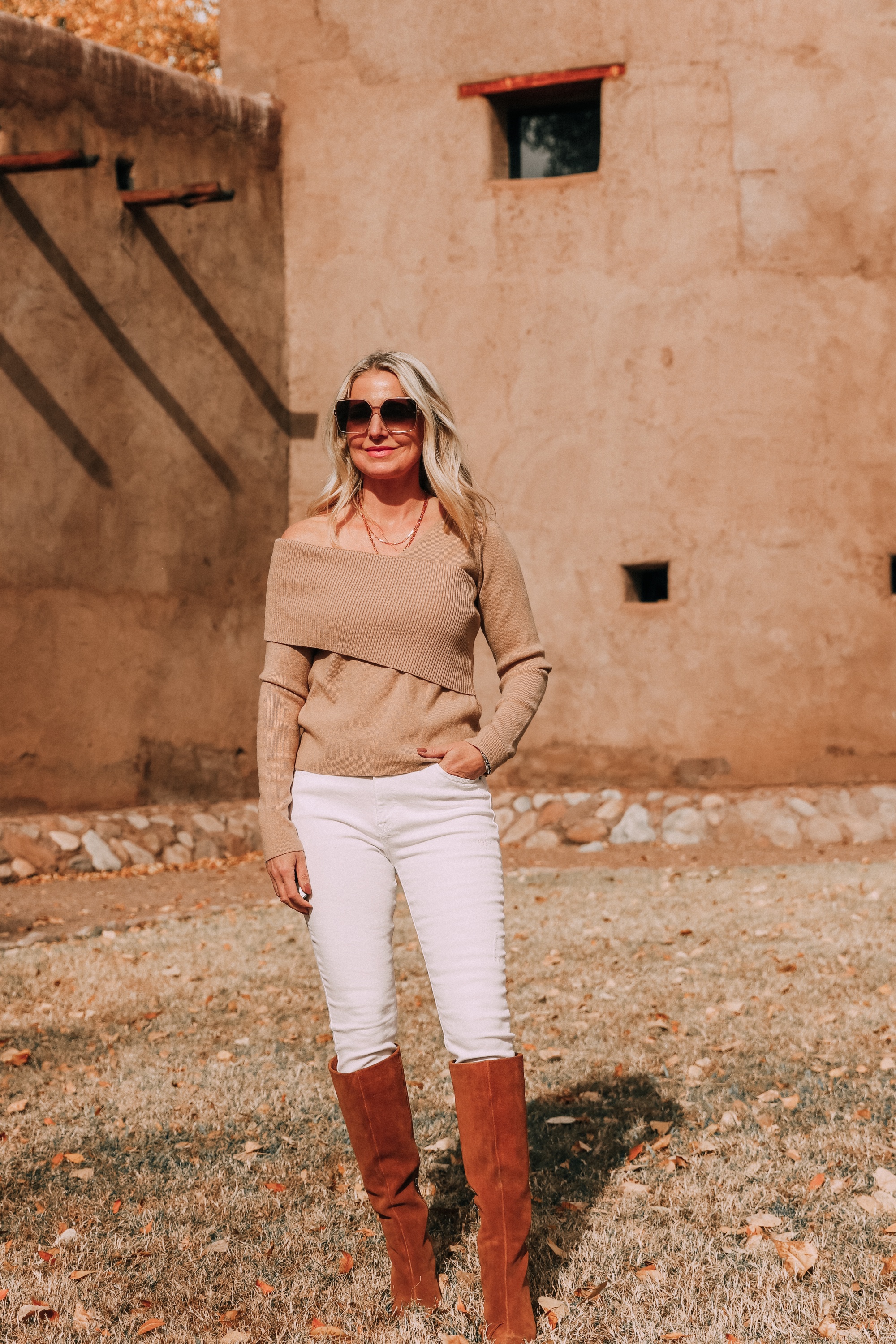 neutral everyday outfit including camel off the shoulder sweater white jeans brown suede cone heel boots