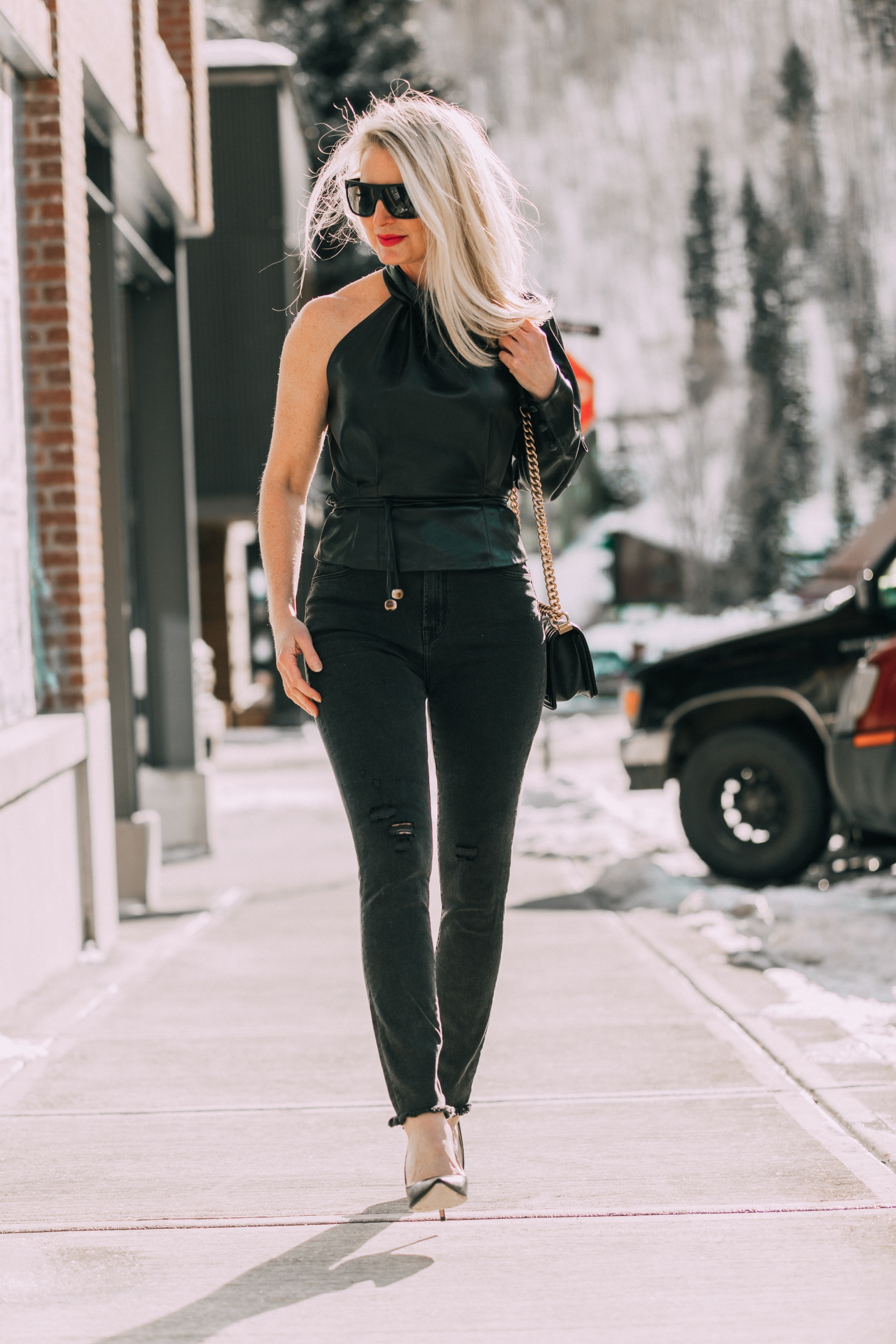 Date Night Outfits, Modebloggerin Erin Busbee von BusbeeStyle.com trägt schwarze, minimal abgenutzte Jeans, Pumps von Jimmy Choo und ein One-Shoulder-Oberteil aus Kunstleder von Nanushka in Telluride, Colorado
