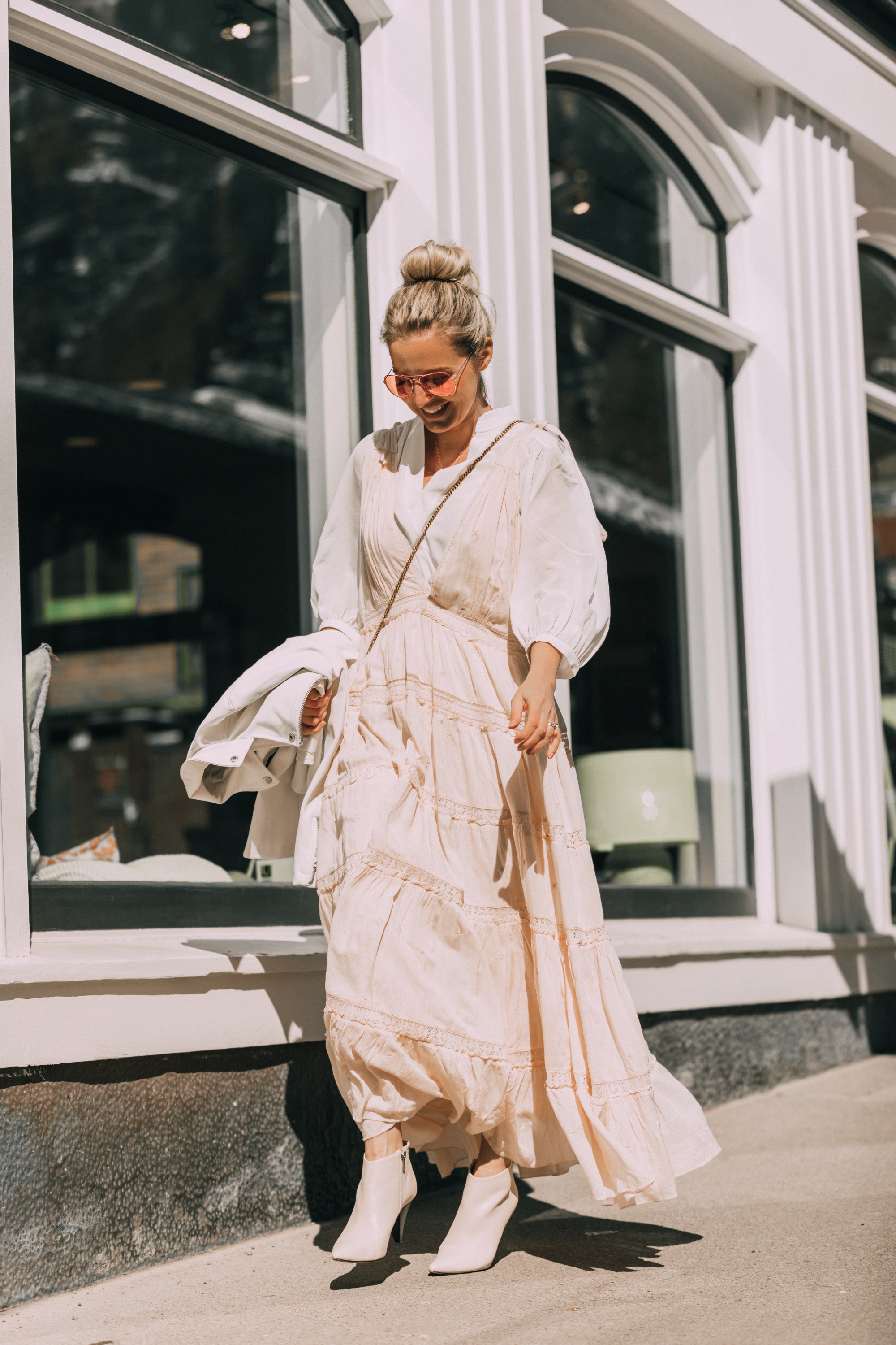 How To Wear A Maxi Dress, Fashion blogger Erin Busbee of BusbeeStyle.com wearing a peach Free People Lily of the Valley Maxi dress over a bubble sleeve white blouse by Frame, white cone heel booties, white crossbody bag, and white faux leather moto jacket from Scoop at Walmart walking in Telluride, Colorado