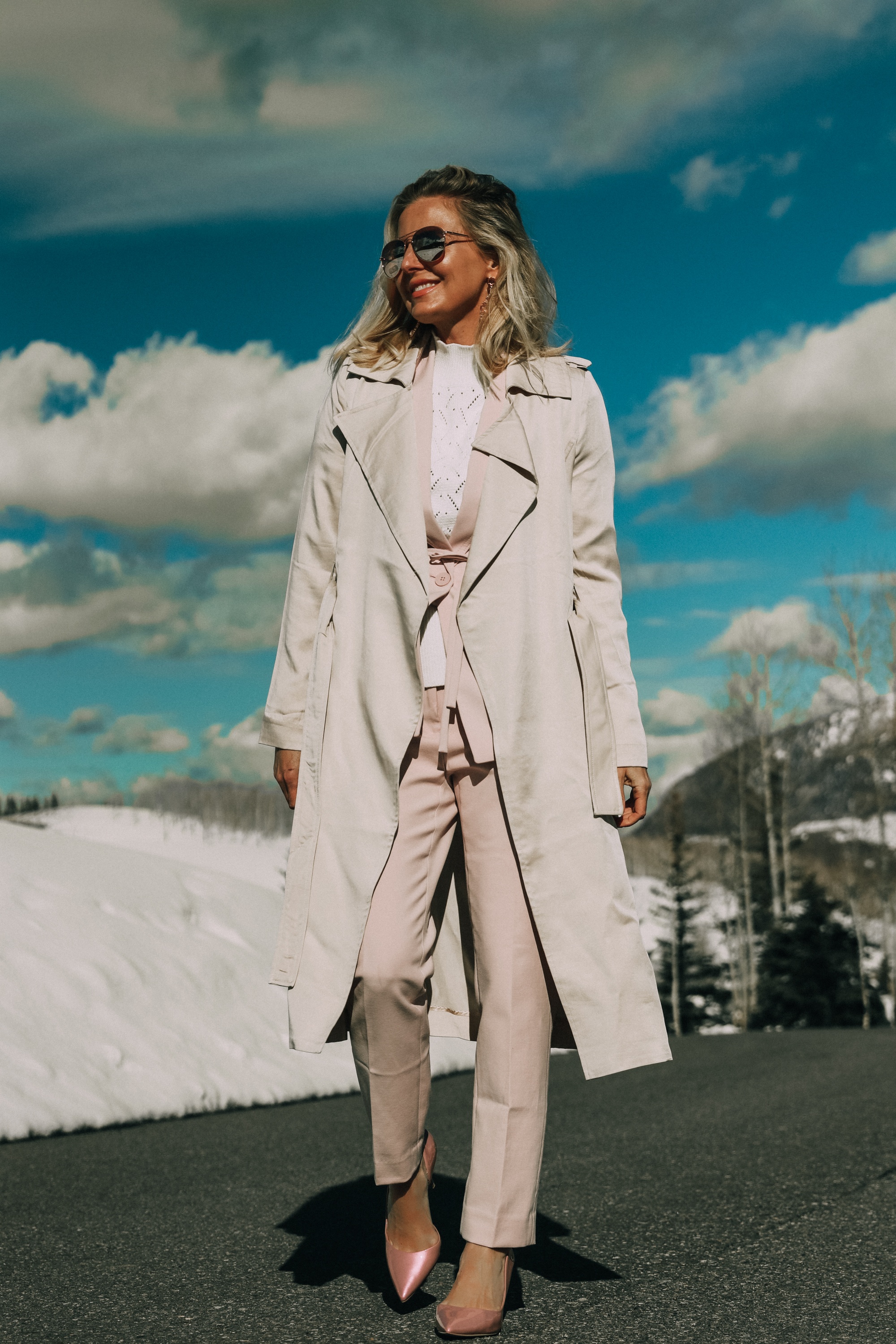 Pink Office Outfit, Fashion blogger Erin Busbee of BusbeeStyle.com wearing a pink power suit from White House Black Market, including a pink belted blazer, pink soft stretch pants, white puff sleeve sweater dress, pink pumps, pink earrings, and aviator sunglasses, and a tan lightweight trench in Telluride, Colorado