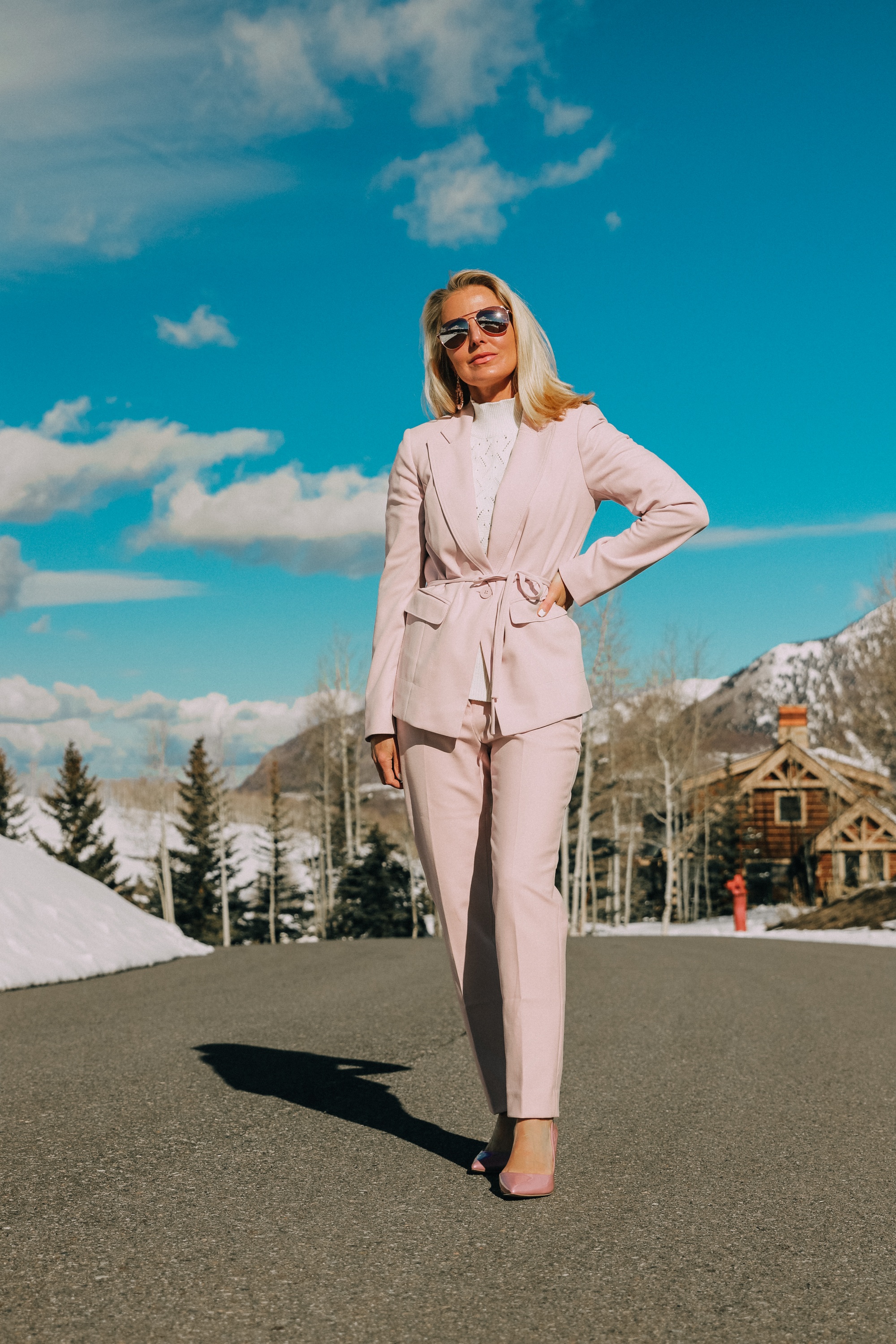 Pink Office Outfit, Fashion blogger Erin Busbee of BusbeeStyle.com wearing a pink power suit from White House Black Market, including a pink belted blazer, pink soft stretch pants, white puff sleeve sweater dress, pink pumps, pink earrings, and aviator sunglasses in Telluride, Colorado