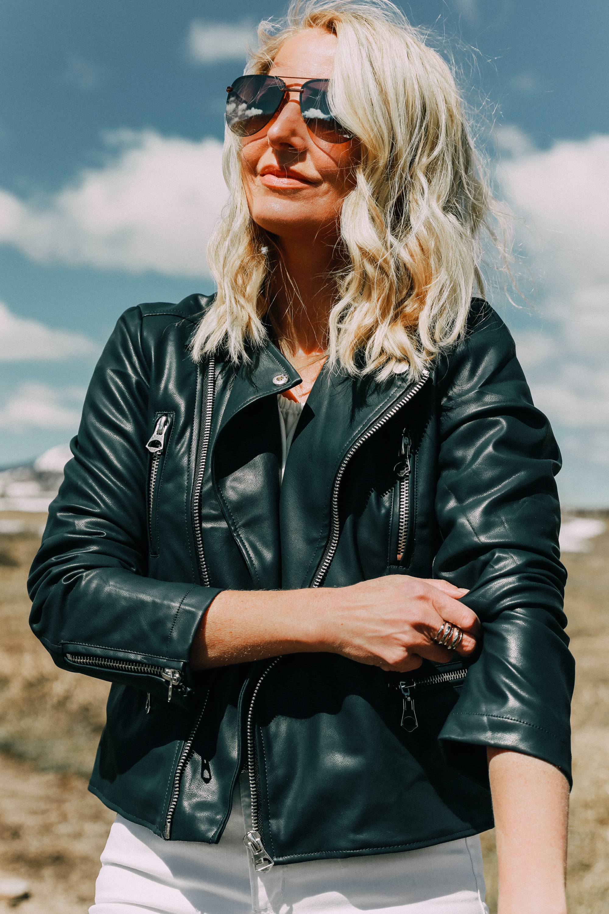Spring style staples, fashion blogger Erin Busbee of BusbeeStyle.com wearing a white bell sleeve off the shoulder blouse under a navy faux leather moto jacket with white kick flare jeans by Scoop from Walmart in Telluride, CO