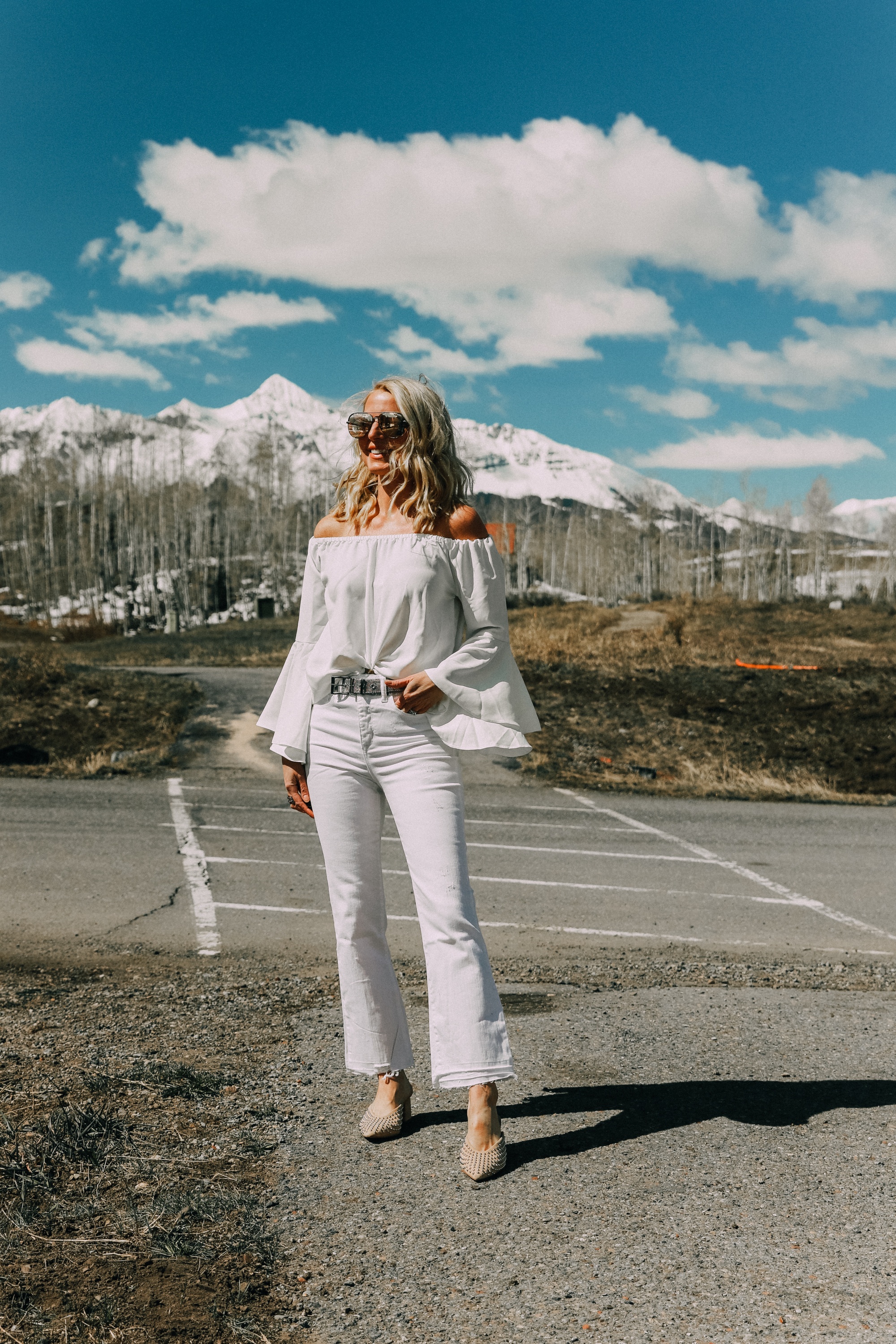 Spring style staples, fashion blogger Erin Busbee of BusbeeStyle.com wearing a white bell sleeve off the shoulder blouse with white kick flare jeans by Scoop from Walmart, and Vince Camuto studded mules in Telluride, CO
