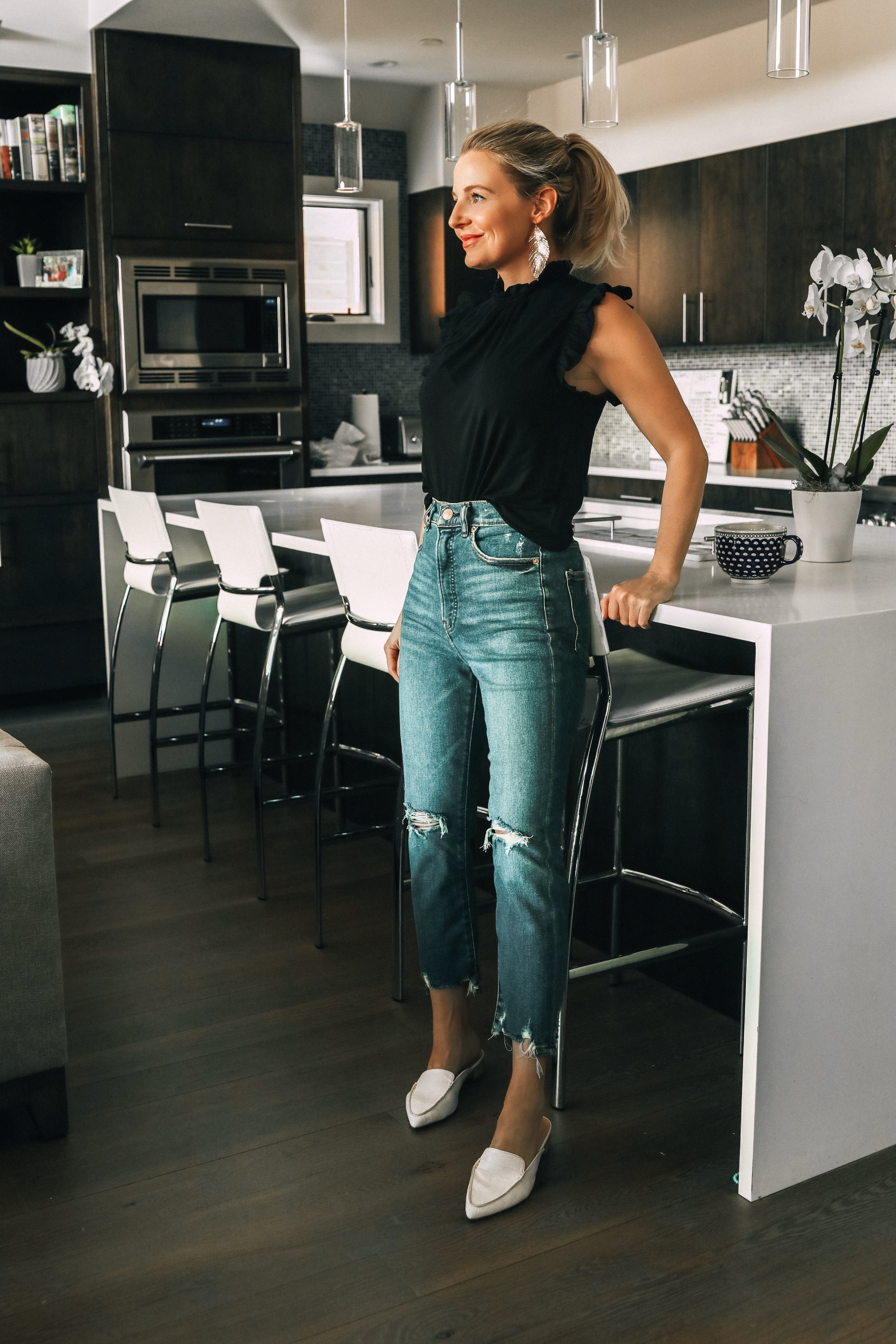 Work from home outfits that are affordable from Express featuring high rise distressed mom jeans, white loafers, black mock neck ruffle cotton top and lightweight leaf earrings