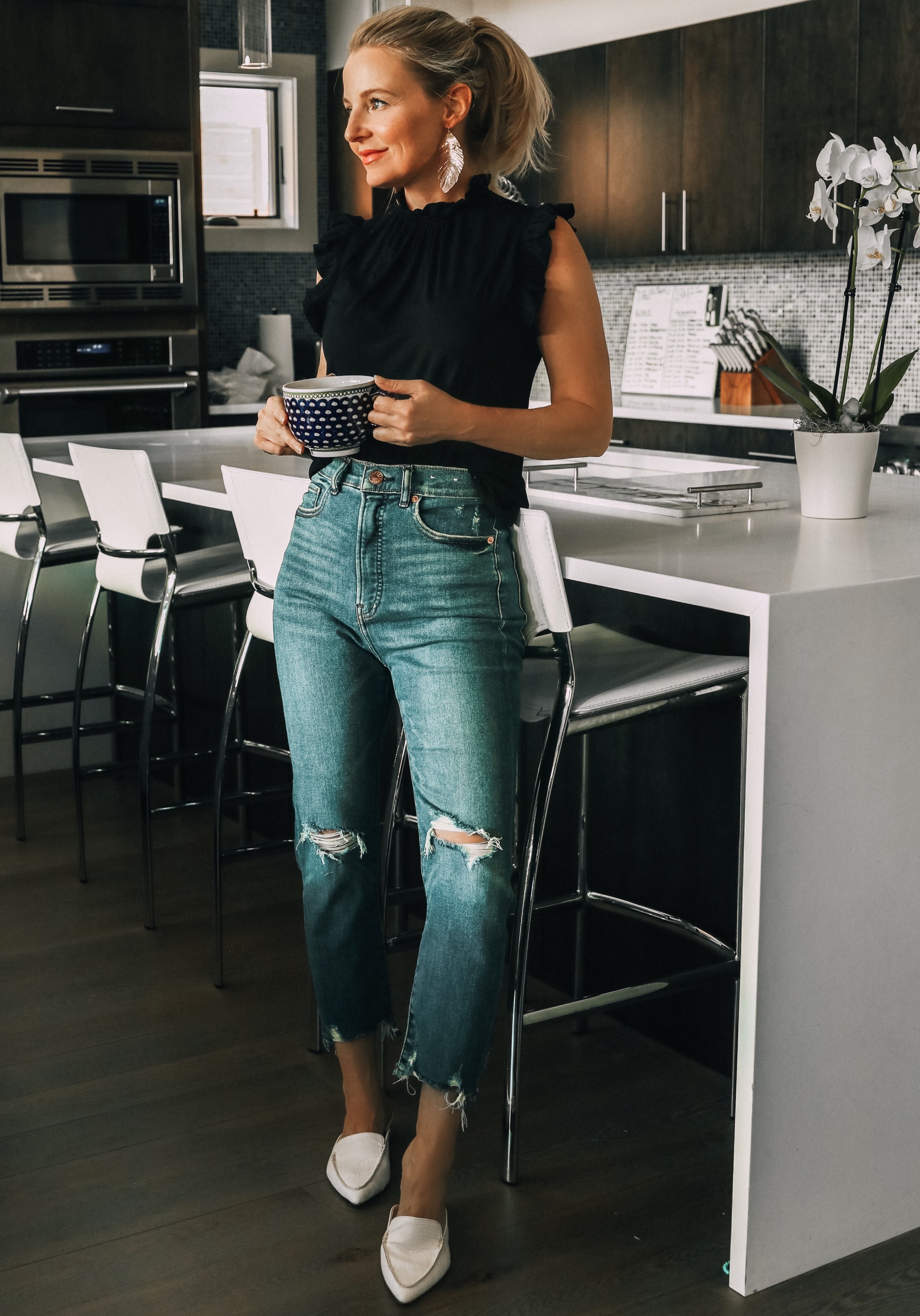 Work from home outfits that are affordable from Express featuring high rise distressed mom jeans, white loafers, black mock neck ruffle cotton top and lightweight leaf earrings
