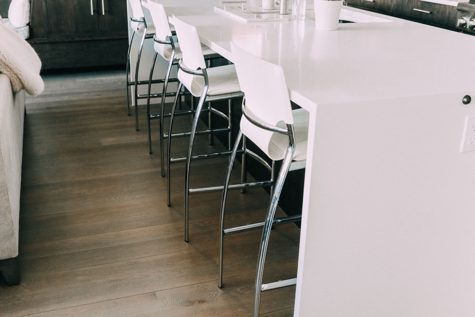 white and chrome kitchen counter bar stools in a row under white waterfall kitchen island