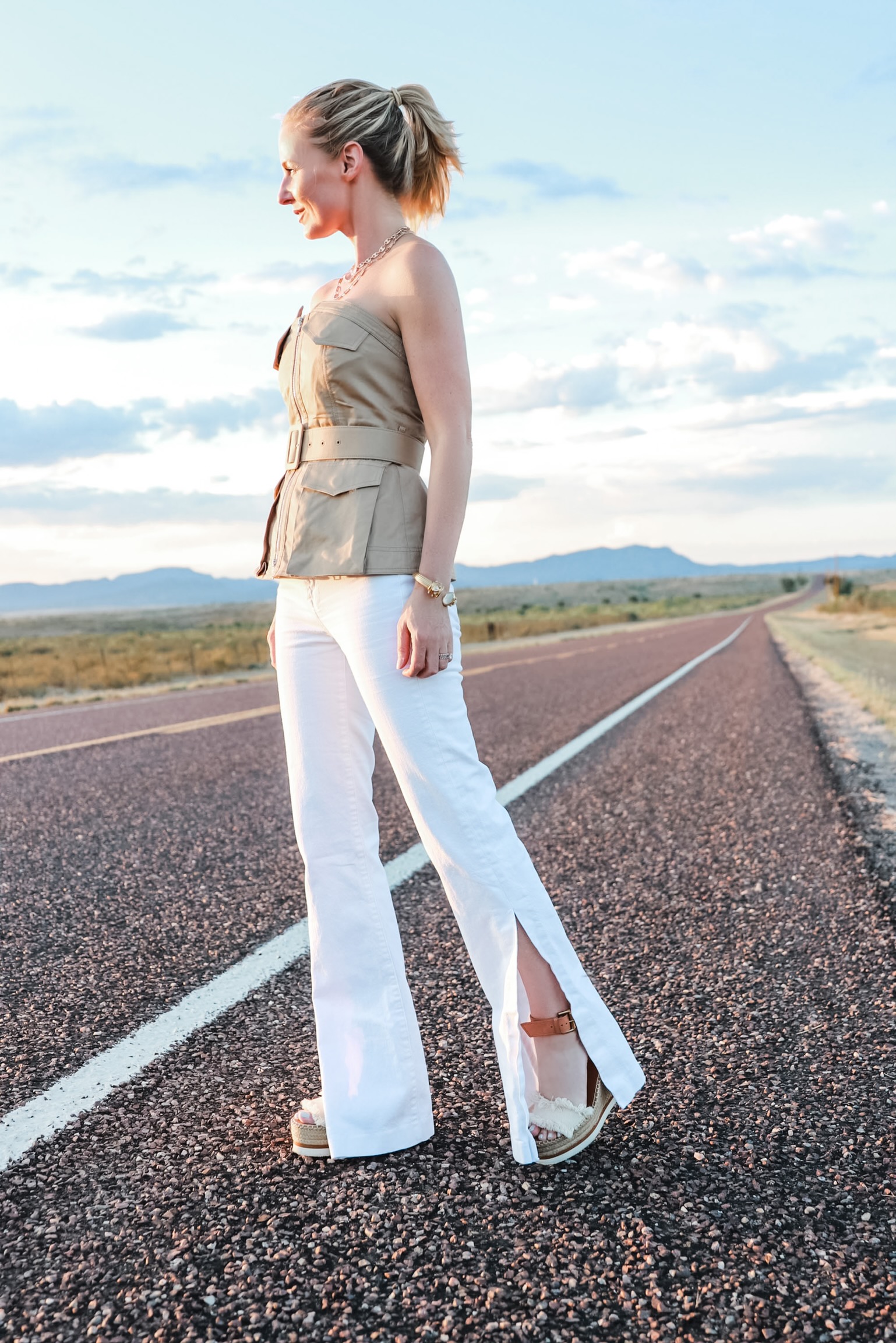 Africa Outfits, Erin Busbee of Busbee Style wearing a tan belted strapless shirt by Self Portrait with white flare jeans and See By Chloe wedges in Texas