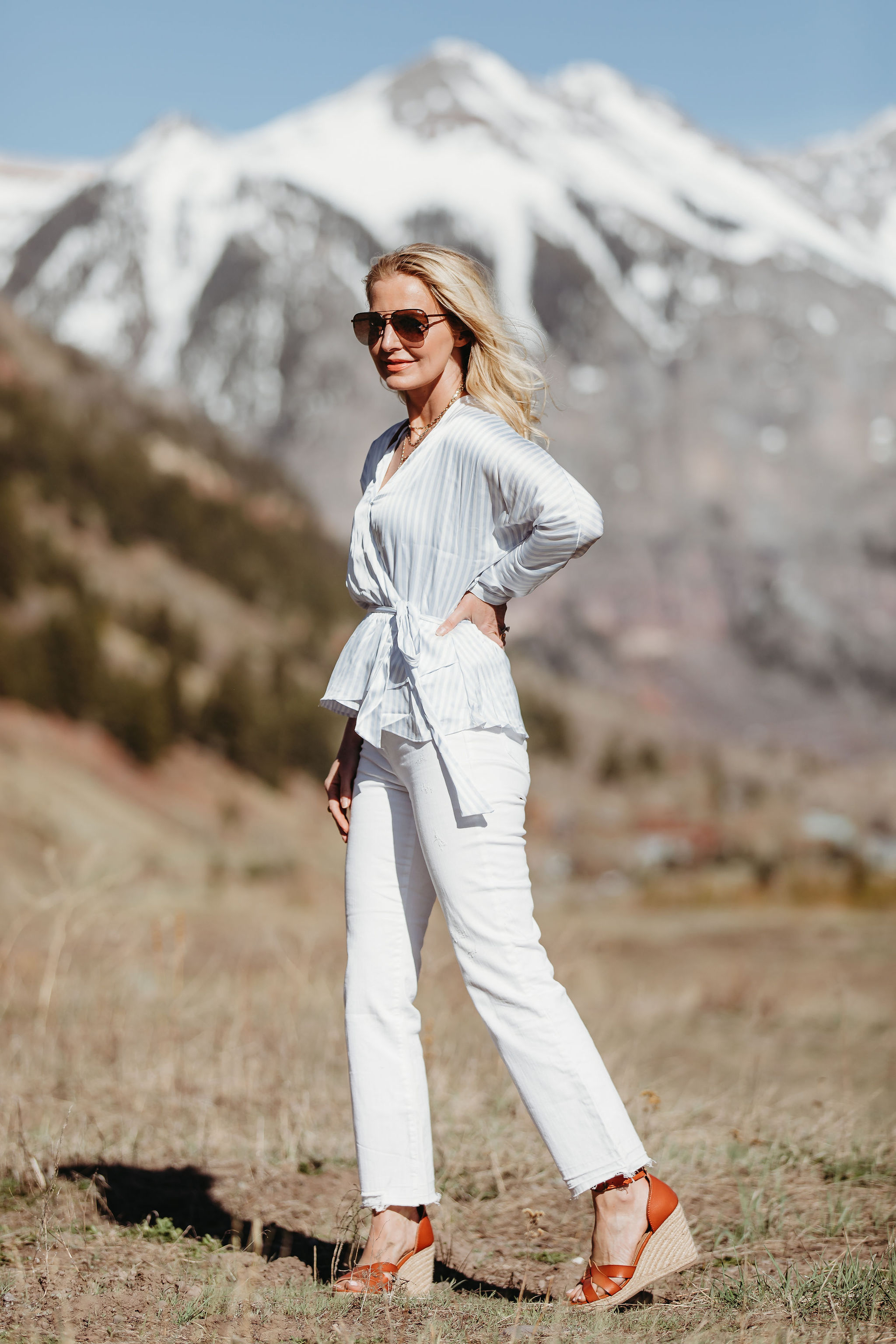 Affordable Summer Tops, Fashion blogger Erin Busbee of BusbeeStyle.com wearing a blue and white striped faux wrap top with white cropped kick flare jeans, straw circle bag, and brown espadrille wedges by Scoop from Walmart in Telluride, Colorado