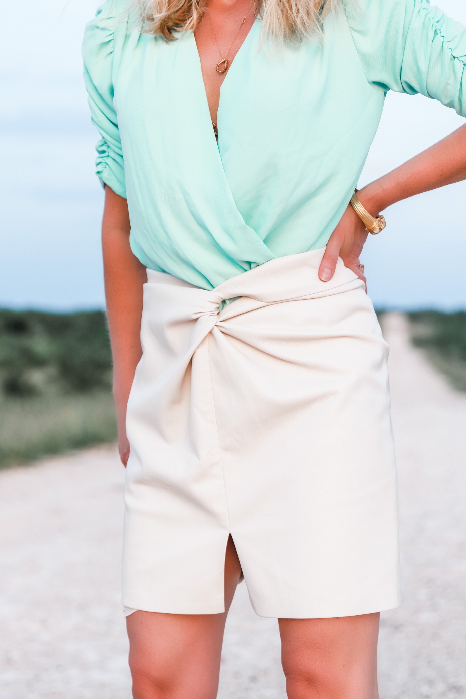 Nanushka Vegan leather Skirt, Fashion blogger Erin Busbee of Busbee Style wearing a mint green bodysuit by Amanda Uprichard, white vegan leather knotted skirt by nanushka, tortoise and pearl earrings by Elizabeth Cole, and white Botega Veneta sandals dupes standing on a ranch in south Texas