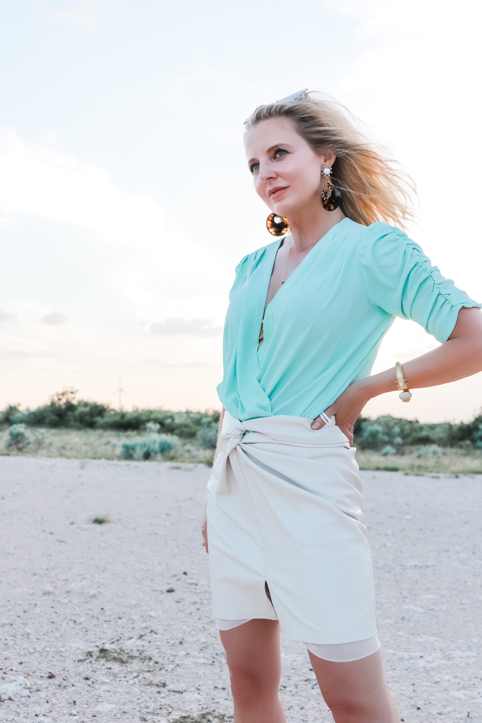 Nanushka Vegan leather Skirt, Fashion blogger Erin Busbee of Busbee Style wearing a mint green bodysuit by Amanda Uprichard, white vegan leather knotted skirt by nanushka, tortoise and pearl earrings by Elizabeth Cole, and white Botega Veneta sandals dupes standing on a ranch in south Texas