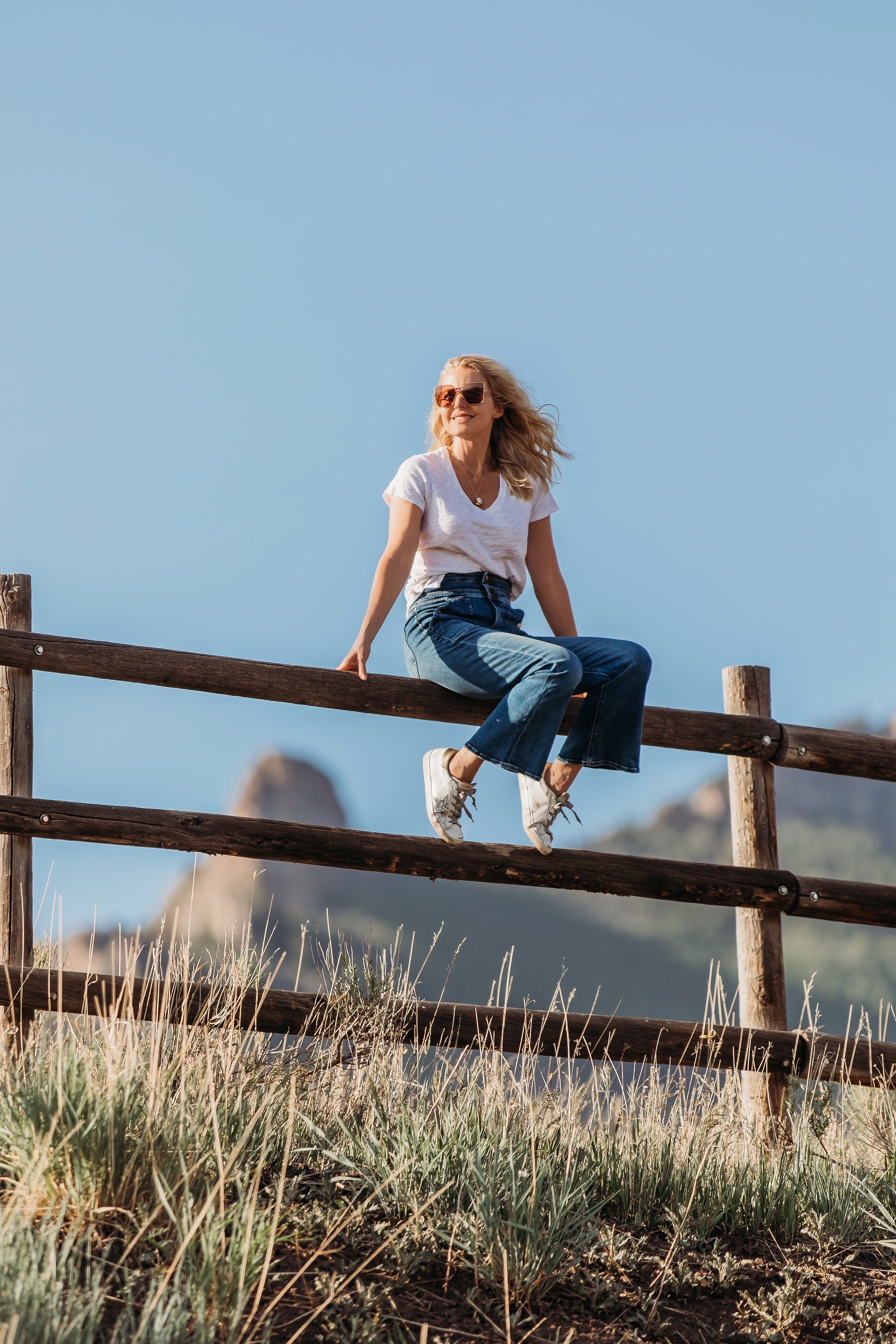 Summer Mom Style, Fashion blogger Erin Busbee of Busbee Style wearing a white v-neck tee with wide leg flare jeans by Frame, Golden Goose sneakers, Julie Vos bracelets, Aligheri necklaces, and Saint Laurent sunglasses in Telluride, Colorado