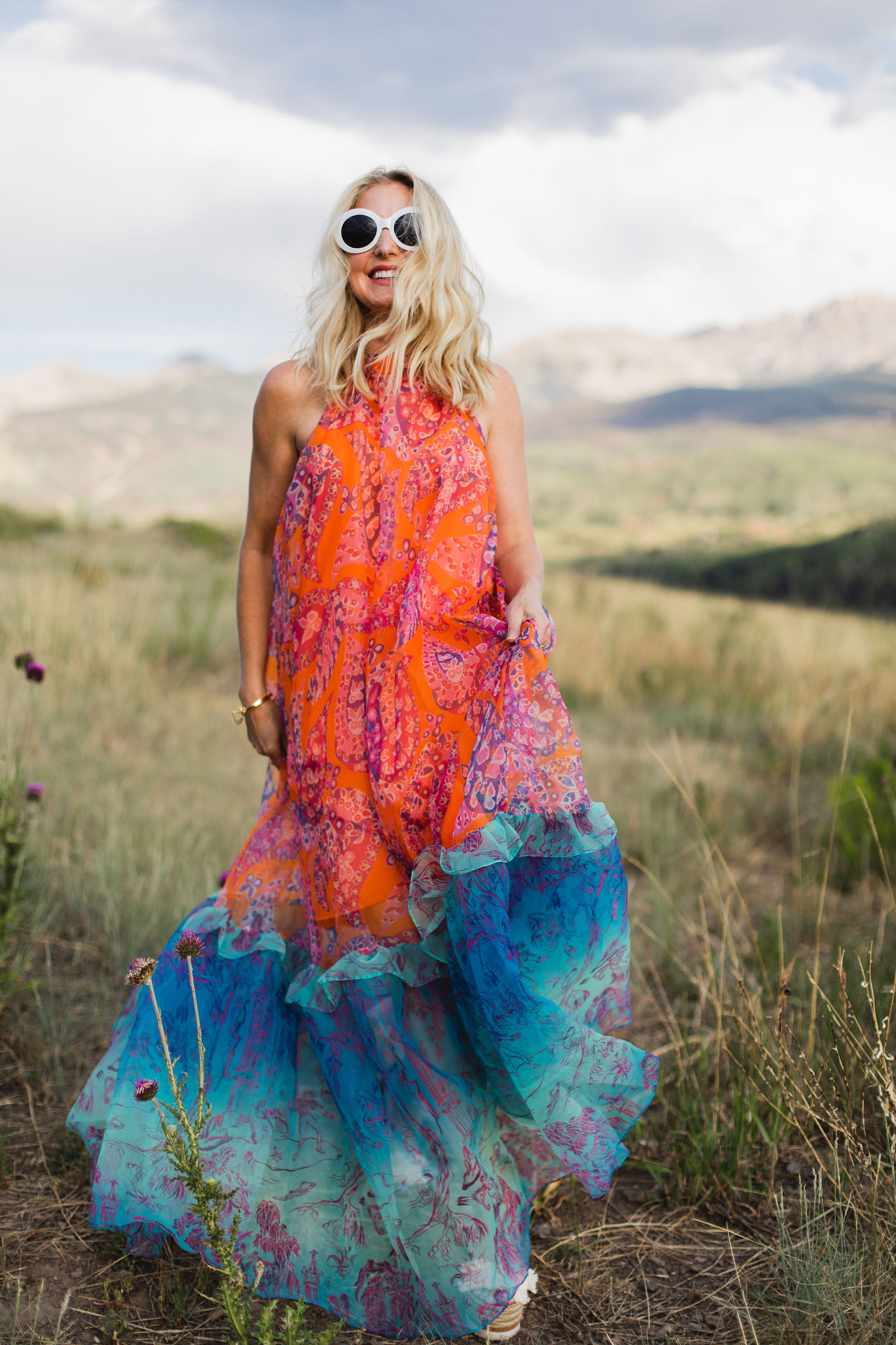 How To Manifest Anything, Modebloggerin Erin Busbee von Busbee Style, trägt ein orange-blaues Kleid von Staud Ina und eine weiße Sonnenbrille und läuft in Telluride, Colorado herum