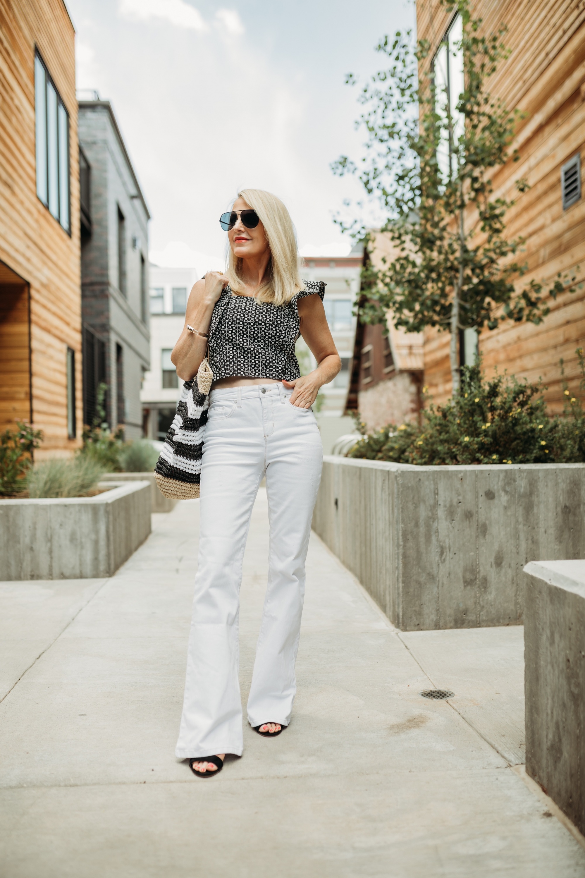 How to Make Legs Look Longer, Fashion blogger Erin Busbee of Busbee Style wearing white flared jeans, printed ruffle sleeve top, black strappy block heel sandals, and striped tote bag by Scoop from Walmart in Telluride, Colorado