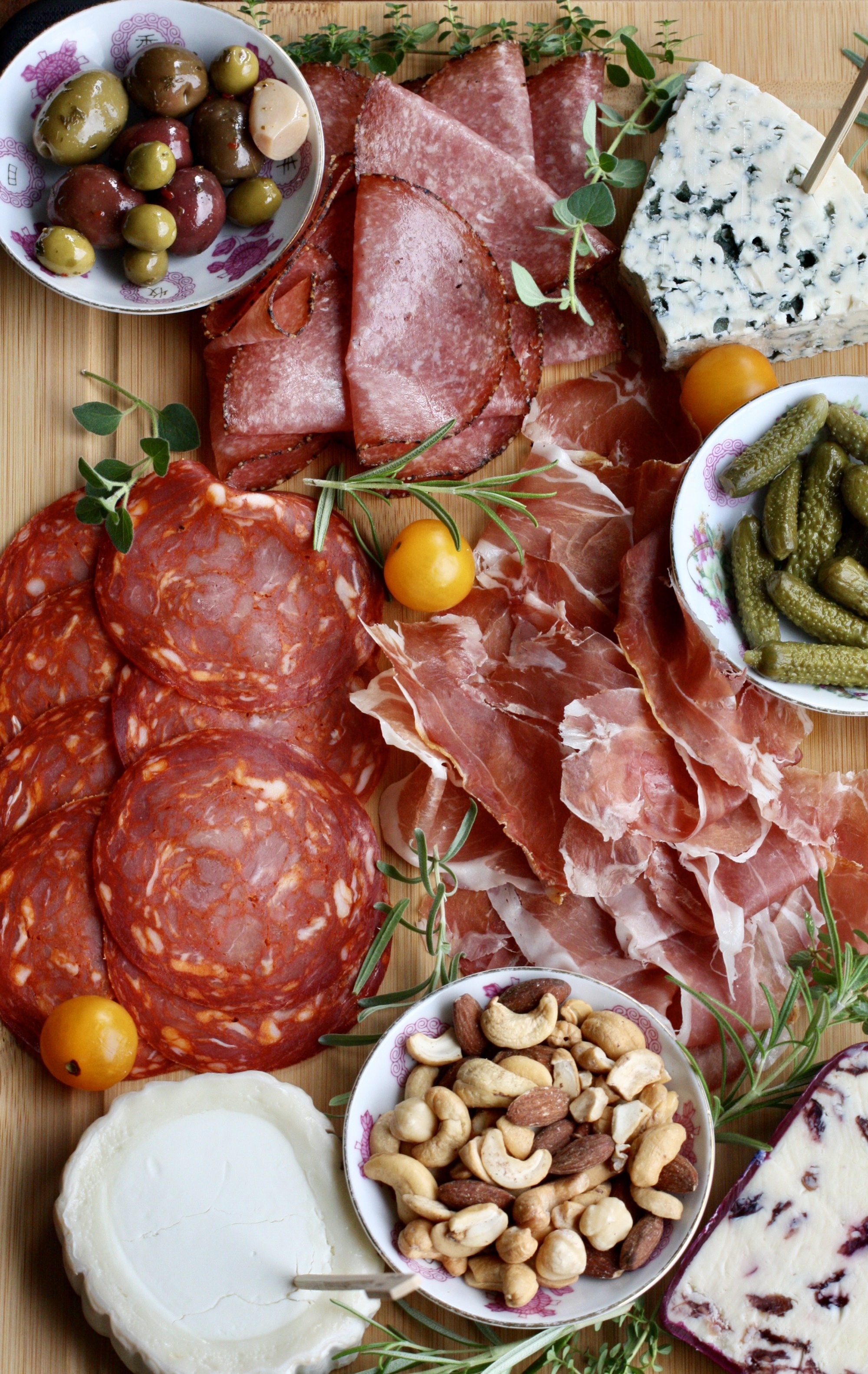 How To Make a Charcuterie Board That Will Wow Your Guests featuring a board full of cured meats, nuts and flavorful cheeses, herb garnishes, cheese board