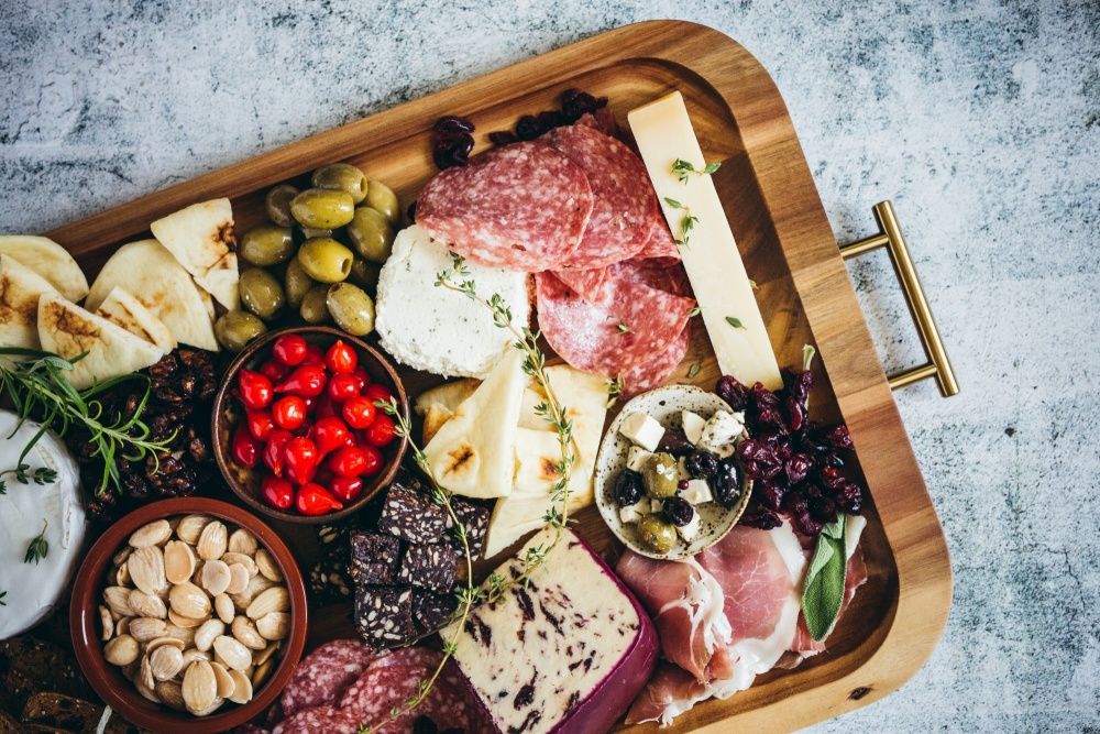 How To Make a Charcuterie Board That Will Wow Your Guests featuring a tray full of cheeses, salami, pita bread, olives, crackers and more, holiday appetizers, cheese board