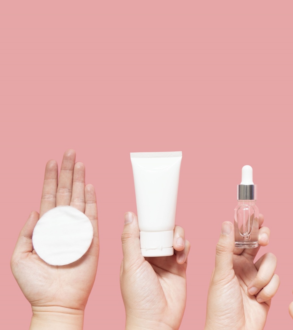 Skin care layer with hands holding up various bottles tubes of products