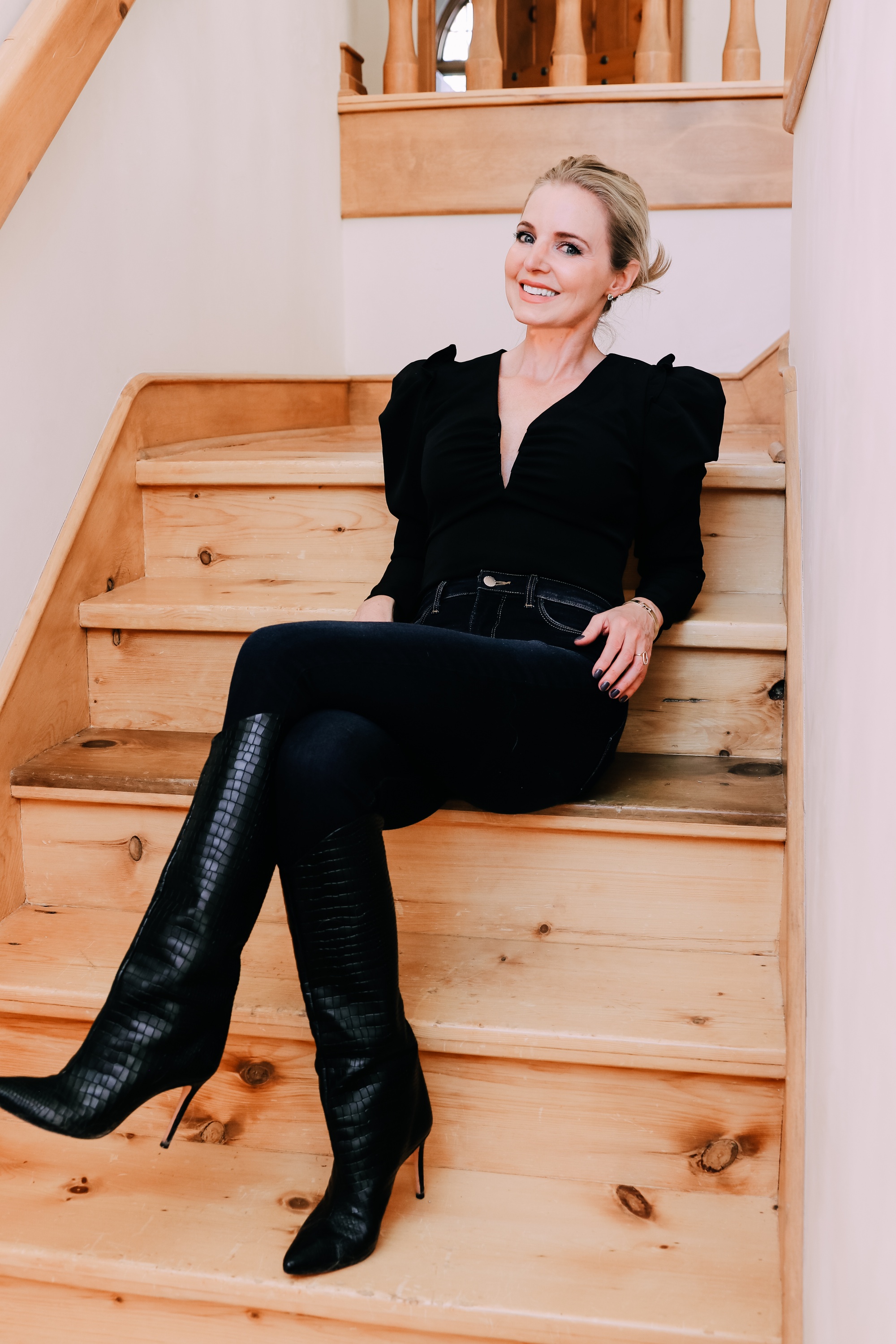 Holiday Outfits With Jeans, Erin Busbee of Busbee Style wearing a black ASTR the Label puff sleeve bodysuit, L'Agence dark wash skinny jeans, and black snake embossed boots by Schutz from Nordstrom sitting on the stairs in Telluride, Colorado