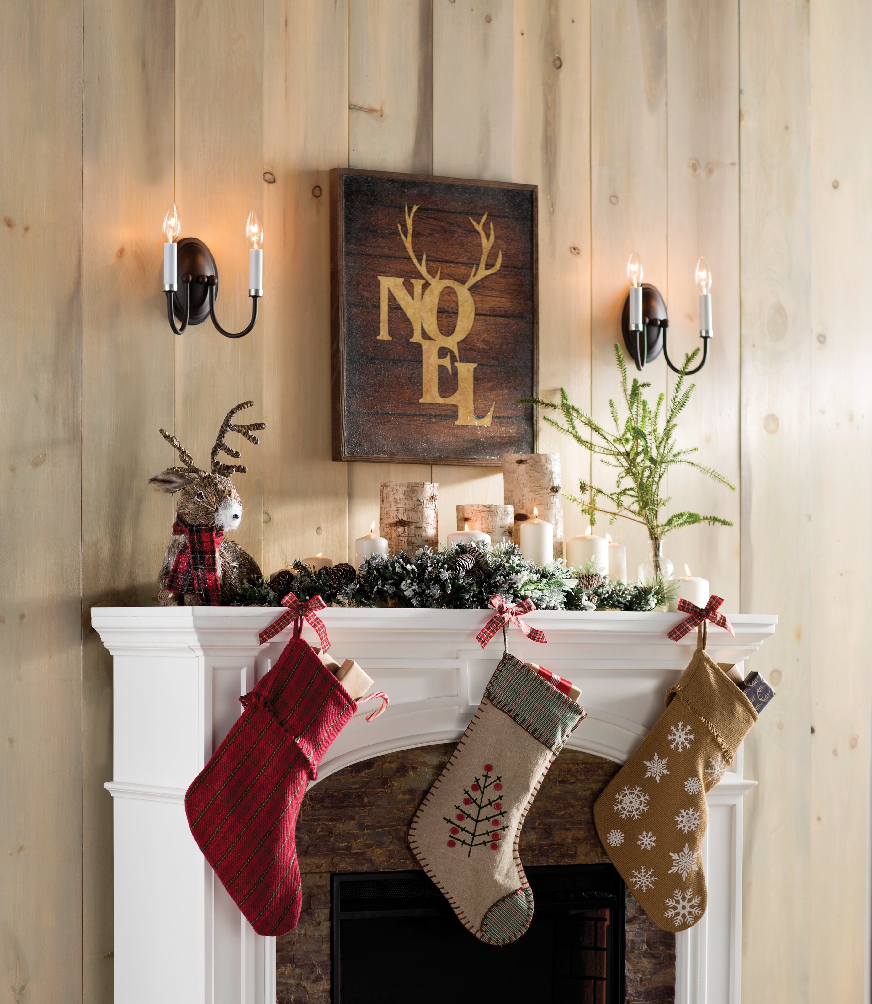 How To Save Time & Money By Repurposing Your Holiday Decor with natural birch hurricane candle holders for your fireplace mantel mixed with white candles, greenery and Christmas stockings